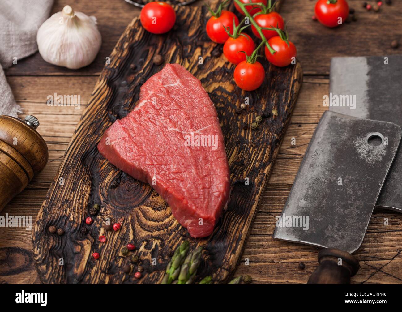 Fetta di manzo crudo sirlion steak sul tagliere di legno con pomodori, aglio e punte di asparagi e carne asce sulla cucina in legno sfondo tabella. Foto Stock