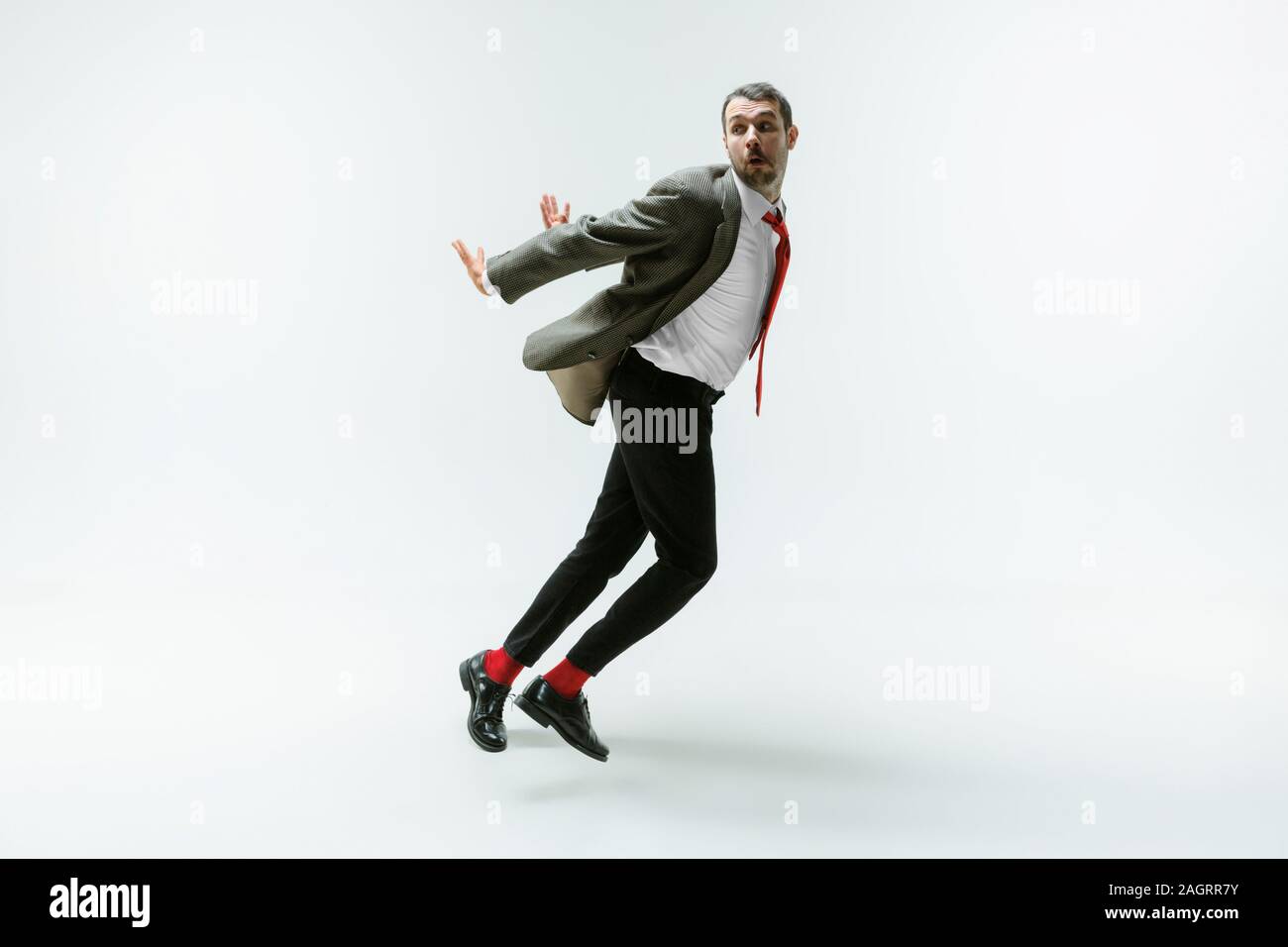 Giovane uomo caucasico flessibili mobili bianco su sfondo per studio. Modello maschile in ufficio wear piegarsi evitando qualcosa, catturato in movimento e di azione. Guarda arrabbiato, spaventata, combattimenti. Emozioni. Foto Stock