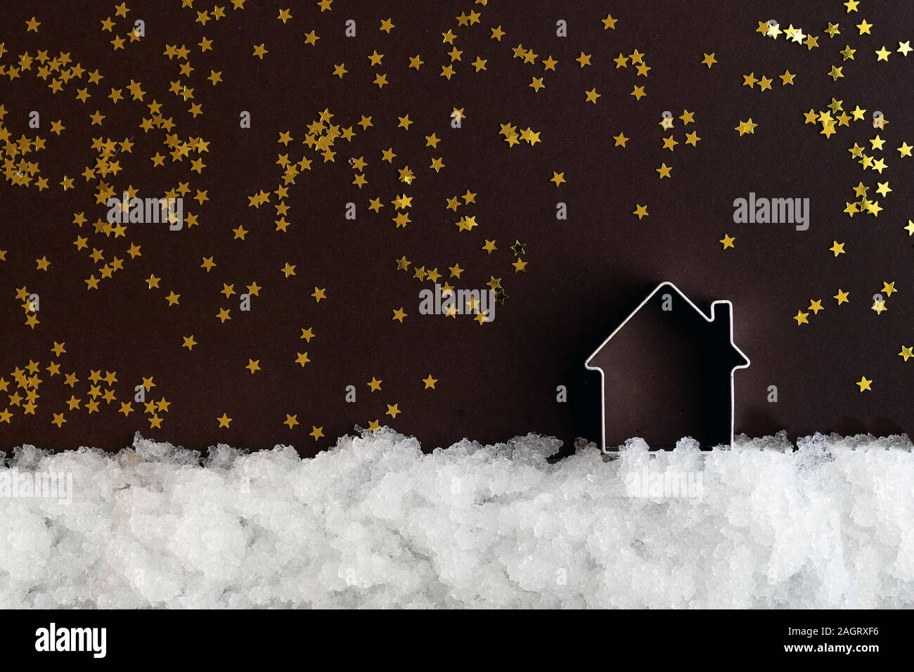 Casa in miniatura sulla neve e uno sfondo scuro con stelle brillanti con copia spazio. Composizione di natale, modello di cartolina Foto Stock