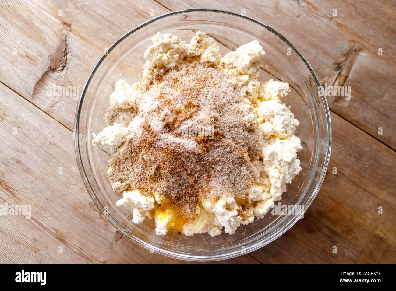 La miscela grezza per la produzione di ricotta torte in recipiente di vetro sul vecchio naturale sfondo di legno vicino la vista. Selective soft focus. Concetto di colazione Foto Stock