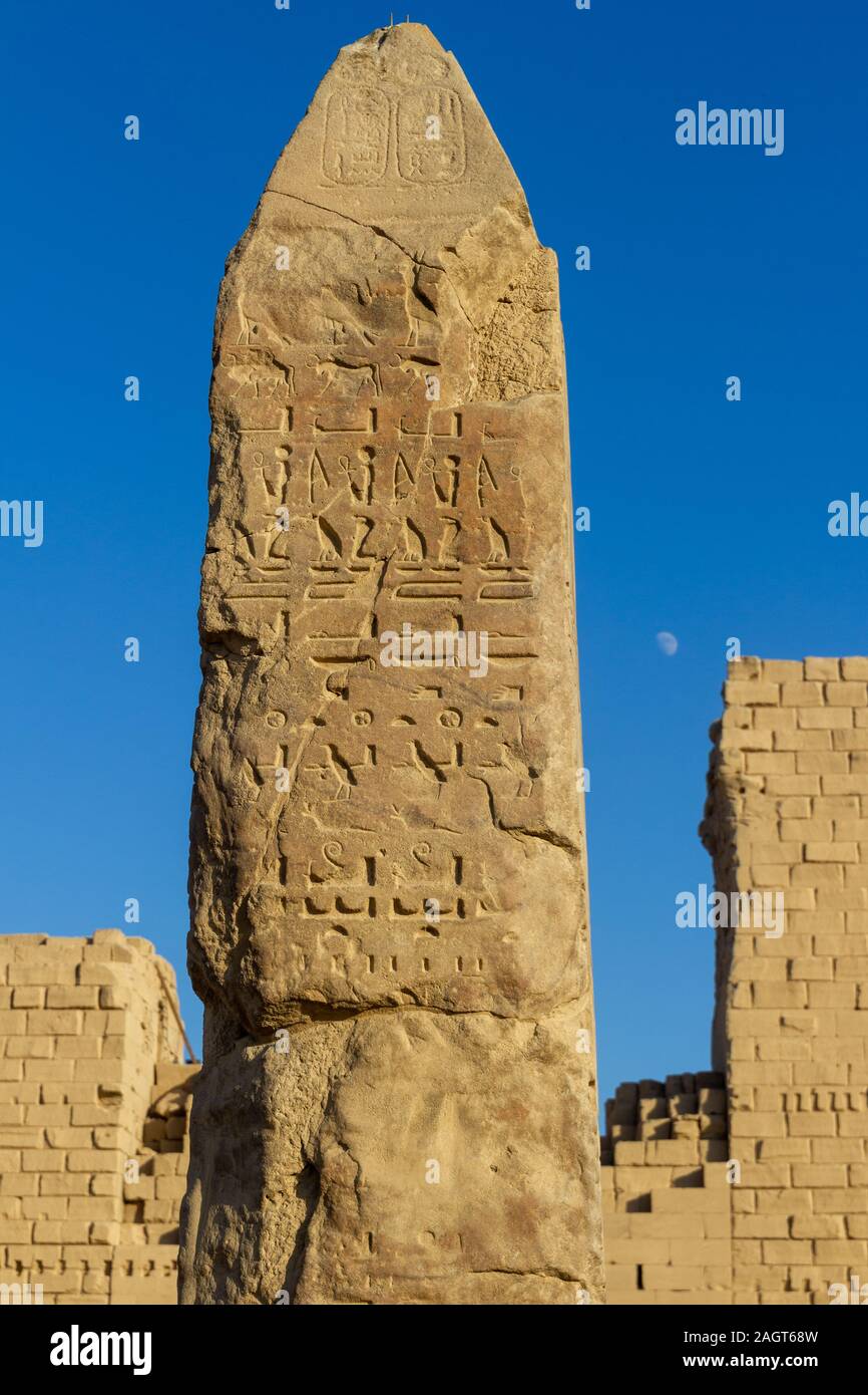 Un obelisco con geroglifici del tempio di Karnak prima di un cielo blu con luna Foto Stock