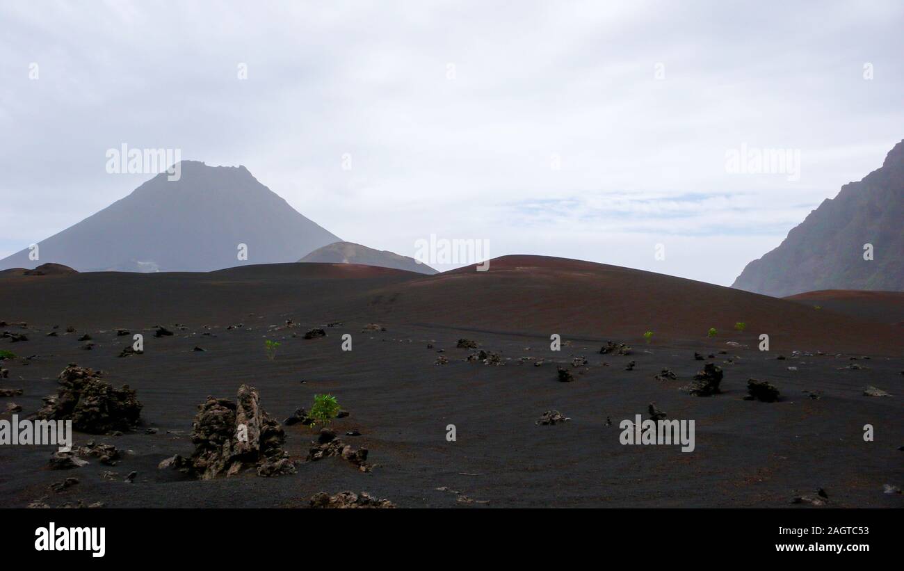 Un stark e desolata vulcano creater paesaggio con lava nera di sabbia e rocce e altri crateri dietro Foto Stock