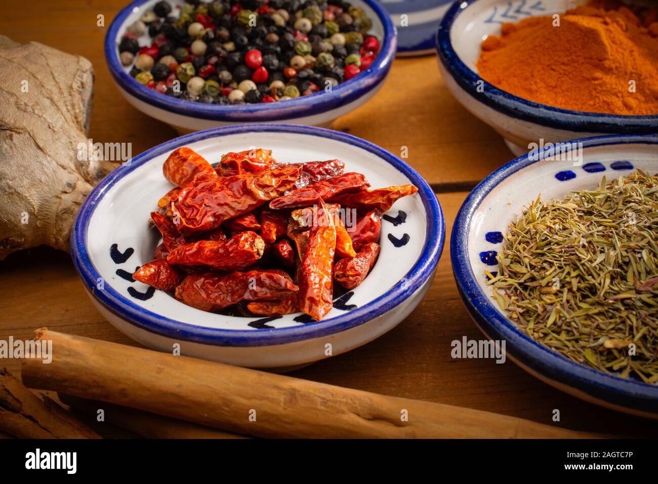 Cibo sano. Le spezie in contenitori in ceramica tipica del Marocco su un vecchio tavolo di legno. Pepe colorati, curcuma, pepe di Caienna, la cannella, lo zenzero e il timo Foto Stock