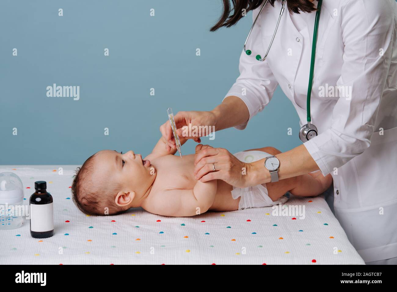 Il bambino si trova sul tavolo e il pediatra misura la temperatura. Foto Stock
