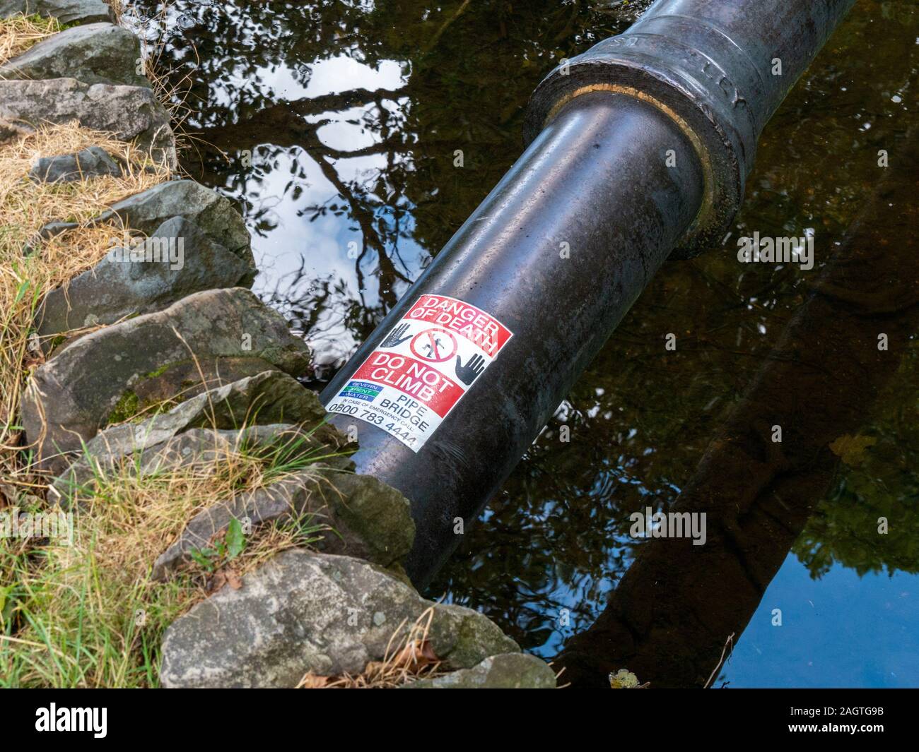 Tubo ponte sul fiume con un cartello di avviso con la dicitura "PERICOLO DI MORTE - Non salire' e simboli, England, Regno Unito Foto Stock