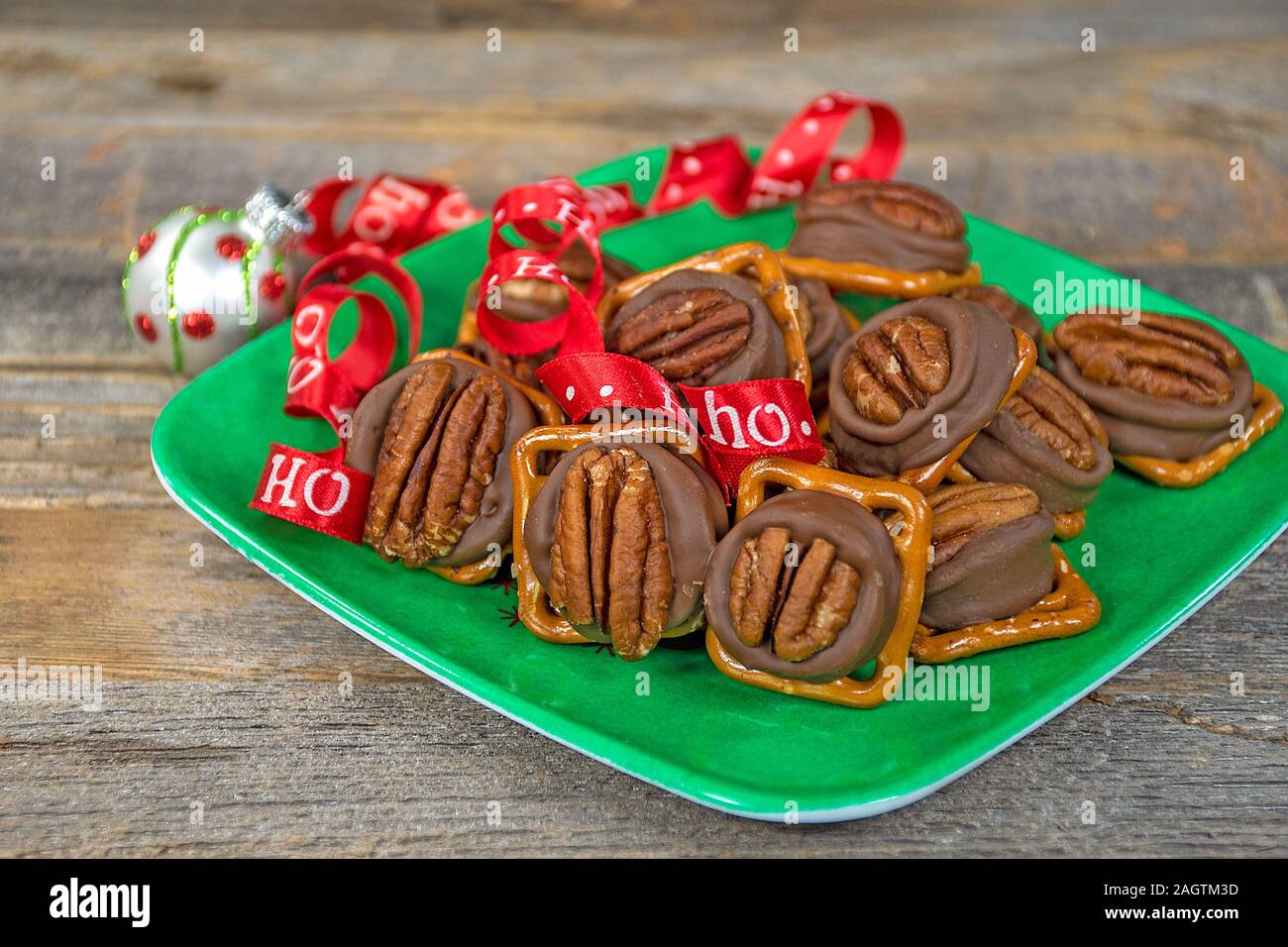 Caramelle di cioccolato fuso su salato pretzel con rosso Natale nastro ed ornamento sul verde della piastra quadrata Foto Stock