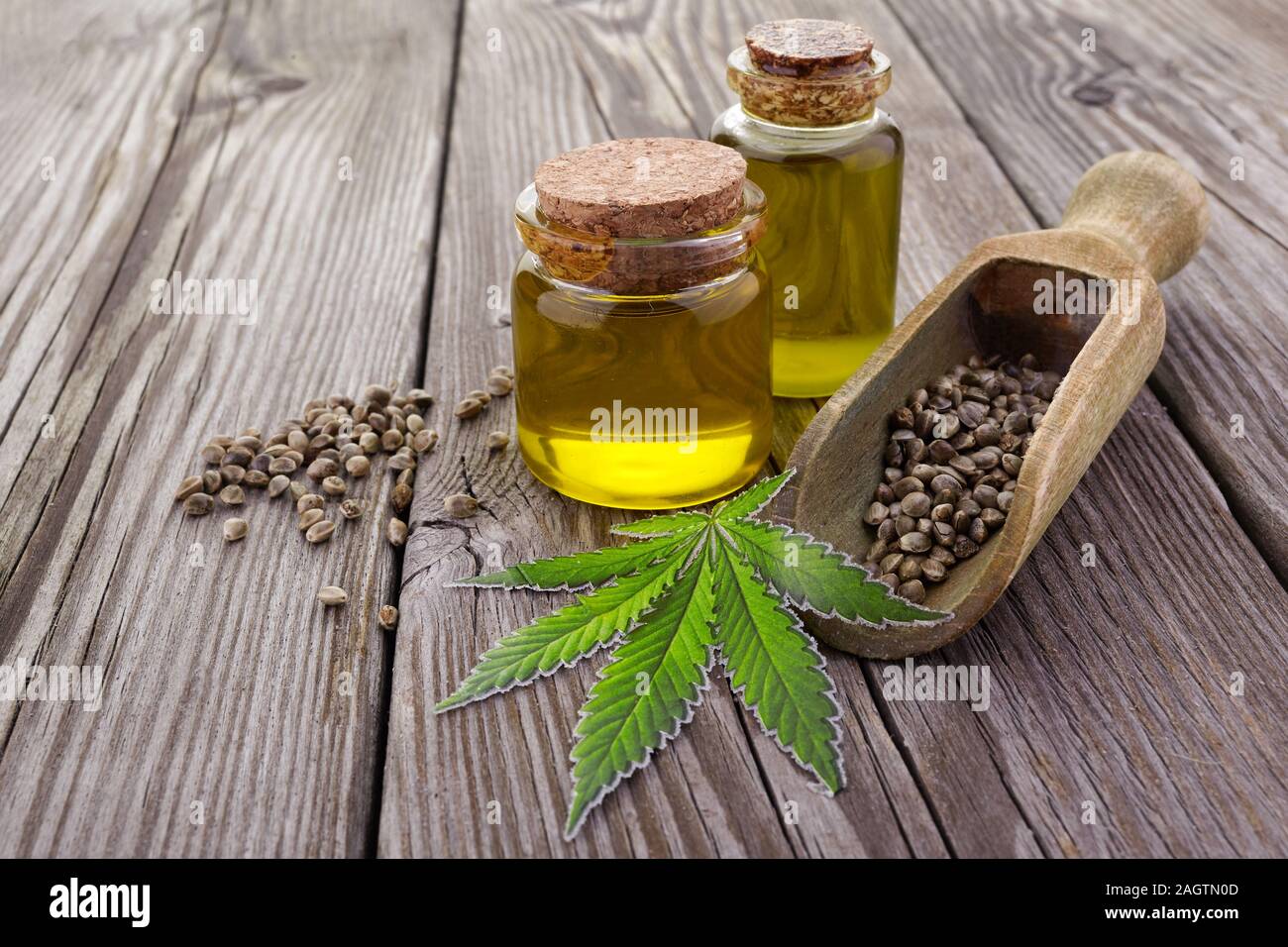 I semi di canapa in cucchiaio di legno, l'olio in un barattolo di vetro, il verde delle foglie di cannabis su sfondo di legno Foto Stock