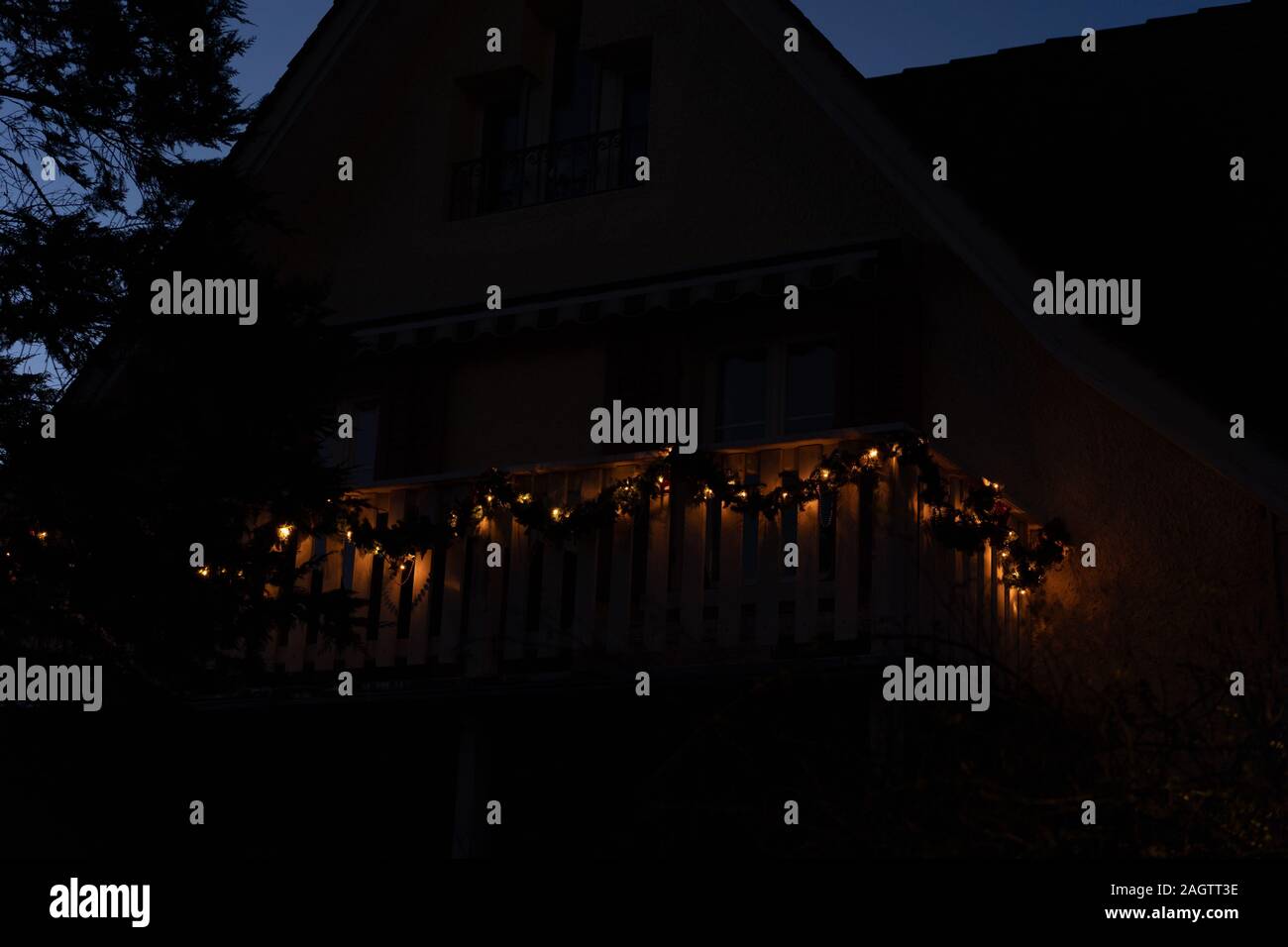 Ghirlande di Natale a lume di candela sul balcone in legno nella parte anteriore di una casa nel crepuscolo a Natale. Albero e casa come una forma. Basso angolo di visione. Foto Stock