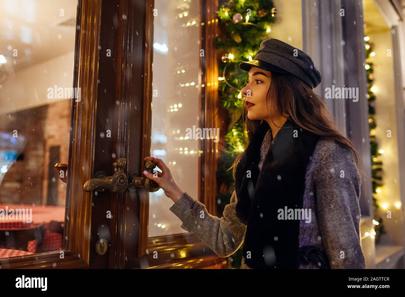 Natale e Anno Nuovo concetto. Donna che cammina sulla strada di città da vetrine decorate. Elegante ragazza guardando alla finestra di vacanza Foto Stock