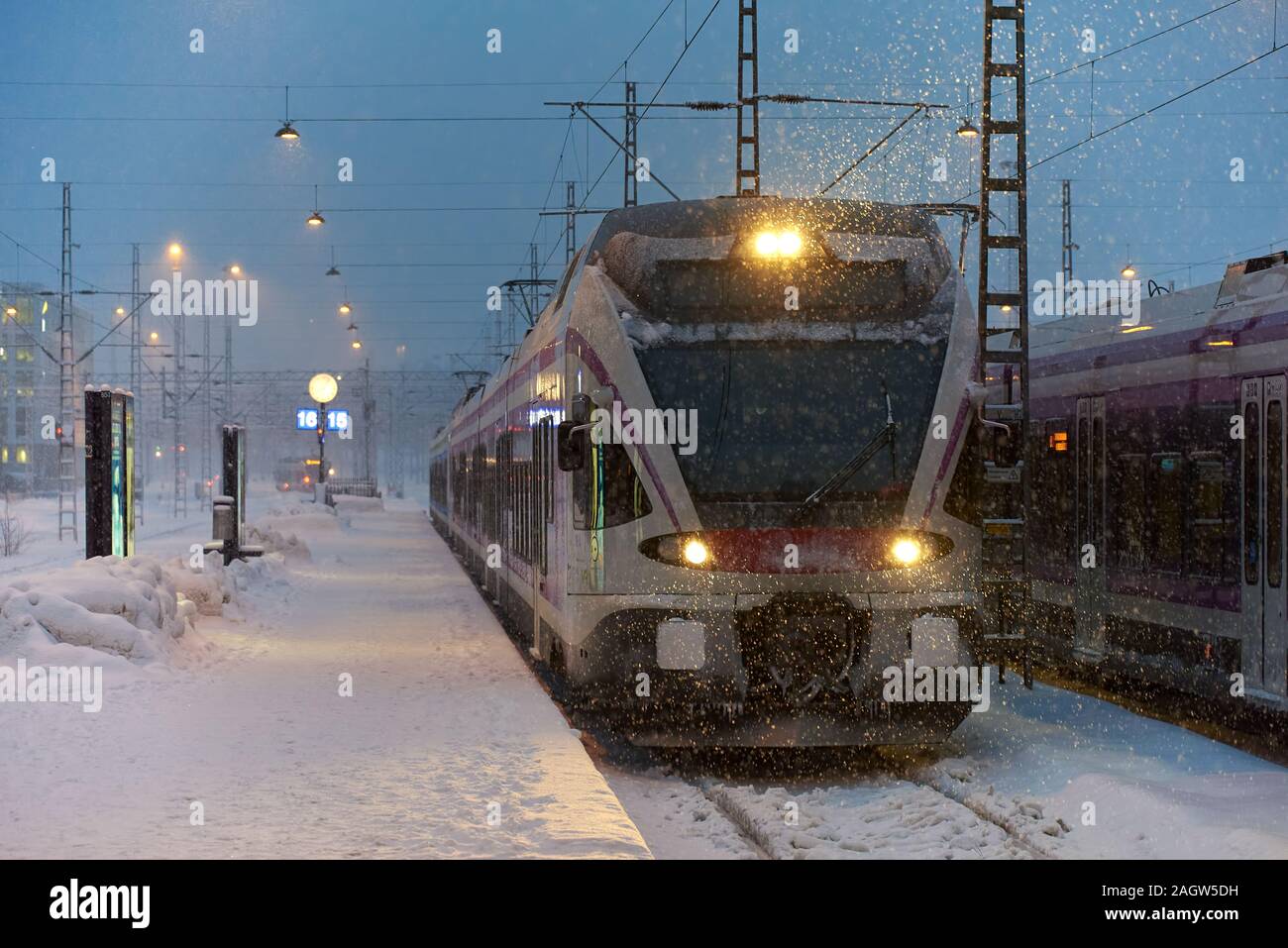 Helsinki, Finlandia - 6 Febbraio 2019: locale treno dei pendolari che arrivano a Helsinki la stazione ferroviaria centrale in pesante tempesta di neve appena prima dell'alba in d Foto Stock