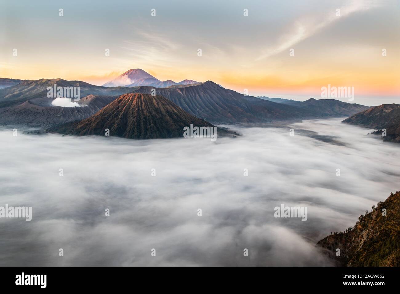 Monte Bromo a sunrise; isola di Giava orientale, Indonesia. Nuvole coperta la valle; fuoriuscite di gas dal cratere. Fumo dal picco vulcanico nel backg Foto Stock