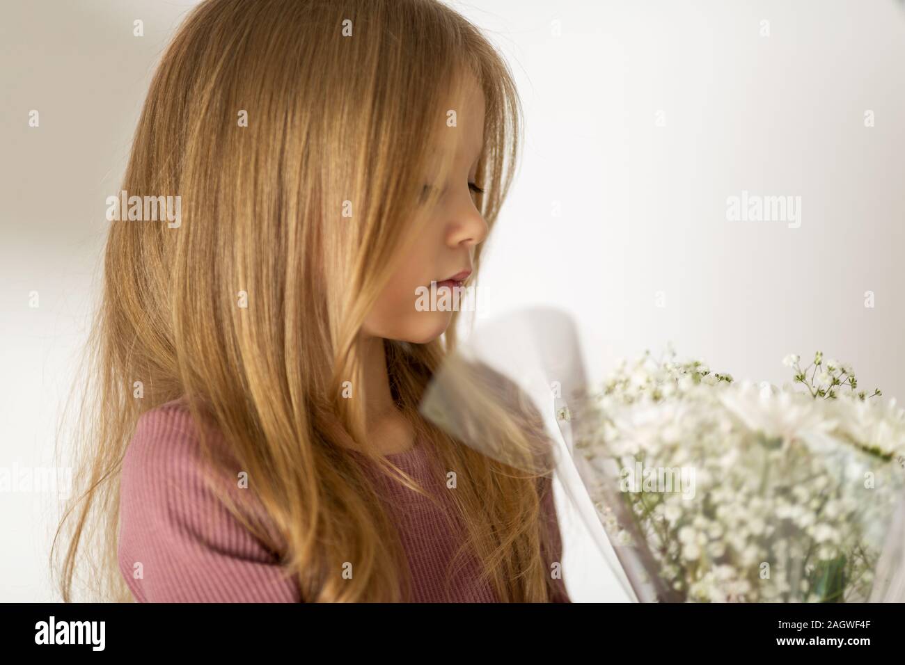 Bella bimba bionda con capelli lunghi tenendo premuto a fondo bianco con un bouquet di fiori. Il concetto di infanzia Foto Stock