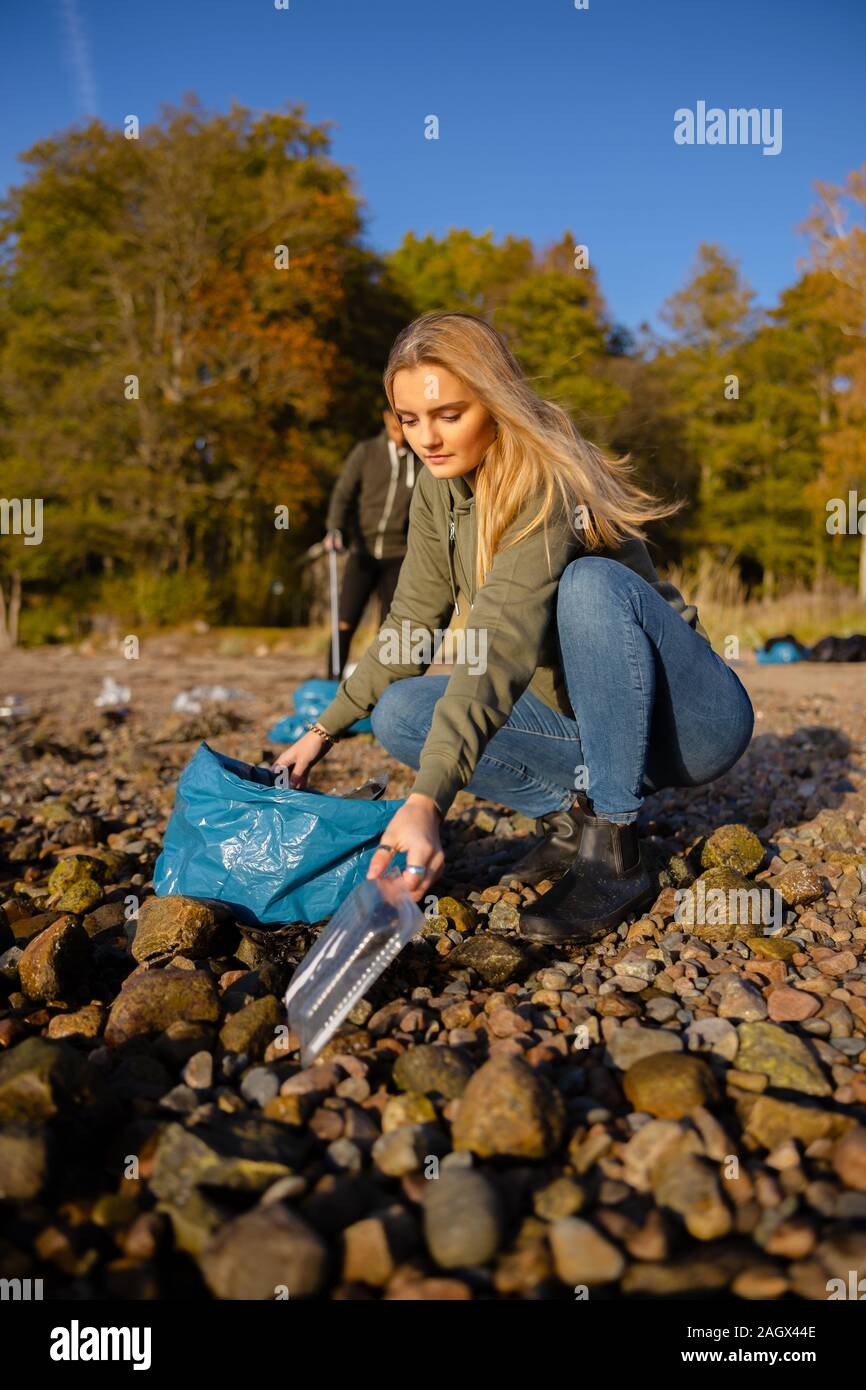 Giovane donna il prelievo di plastica alla spiaggia rocciosa Foto Stock