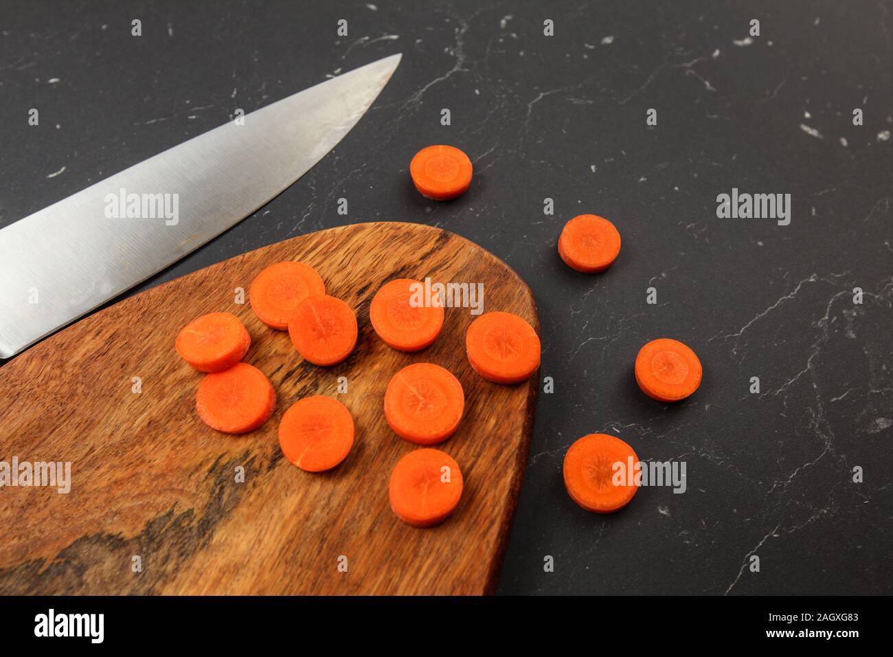 La carota tagliata per piccoli cerchi sul tagliere di legno, chef coltello successivo marmo nero come la scrivania. Foto Stock