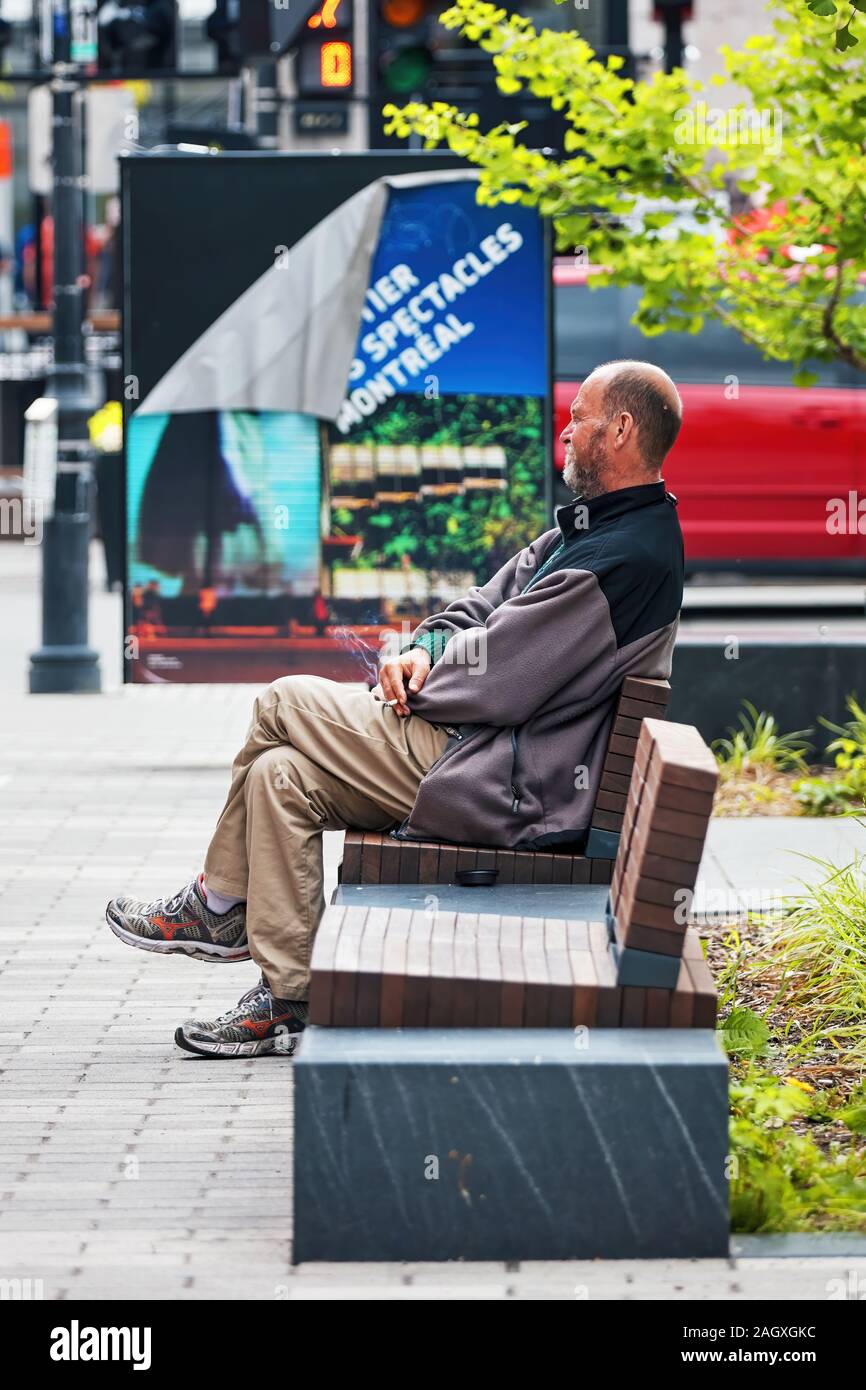 Montreal, Canada - Giugno, 2018: Canadese senzatetto uomo seduto sul banco di lavoro e il fumo di sigaretta. Foto Stock