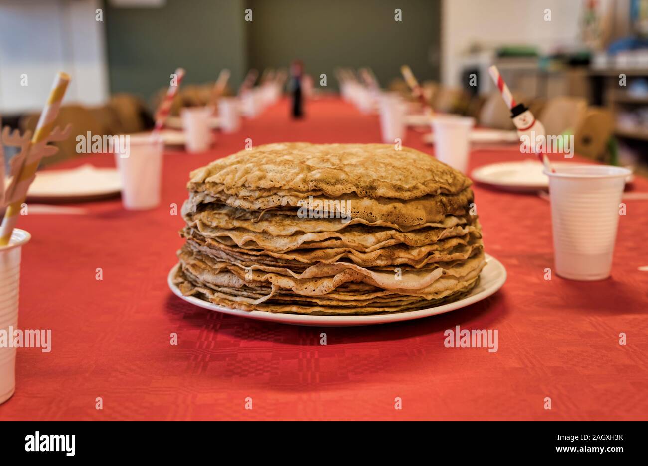 Impostare la tabella con una piastra con una pila di frittelle su una tovaglia rossa con bicchieri per bevande Foto Stock