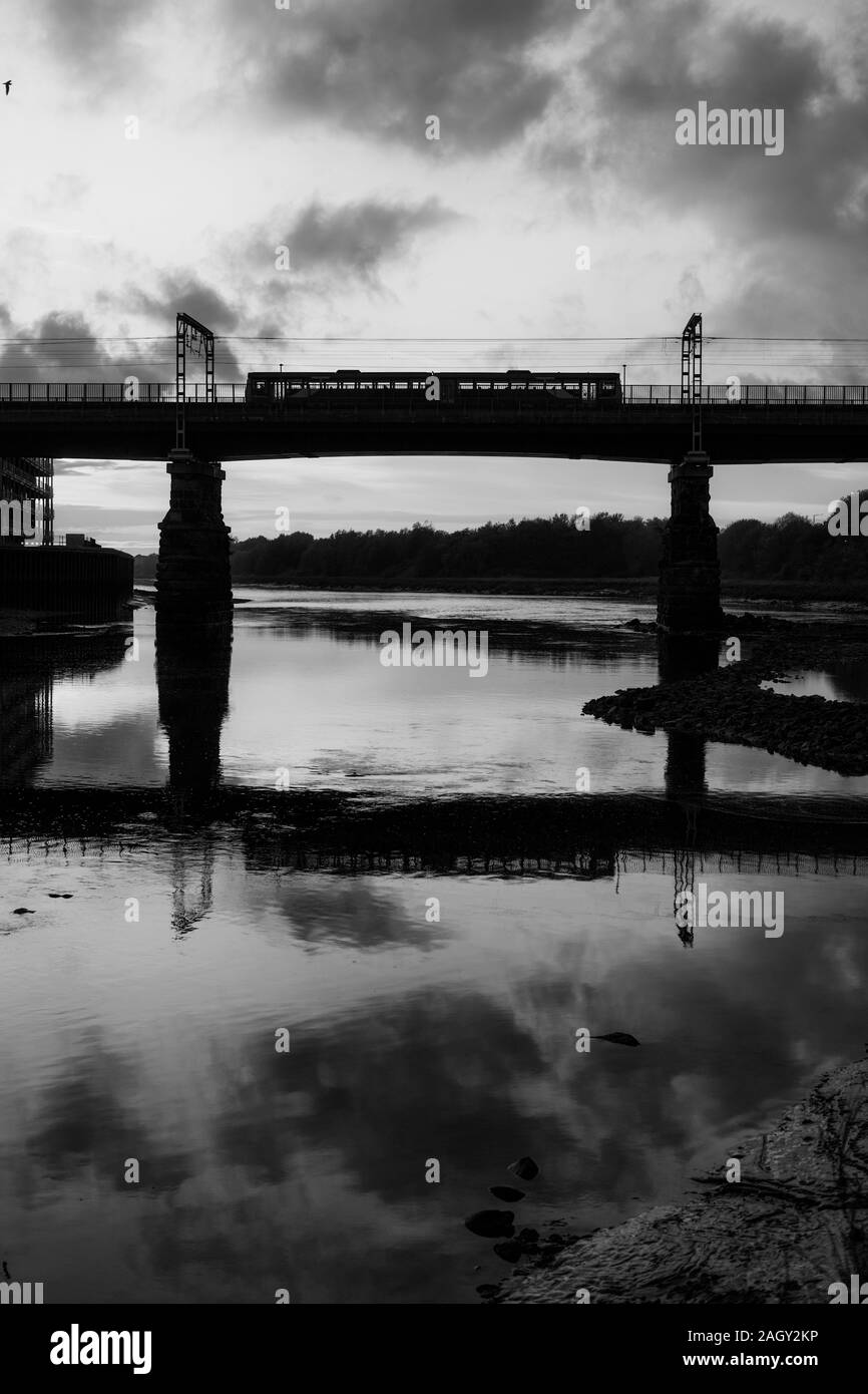 Arriva Nord classe rampa 142 treno pacer attraversando il ponte di Carlisle, Lancaster (fiume Lune) riflesso nel fiume rendendo un tramonto sillhouette Foto Stock