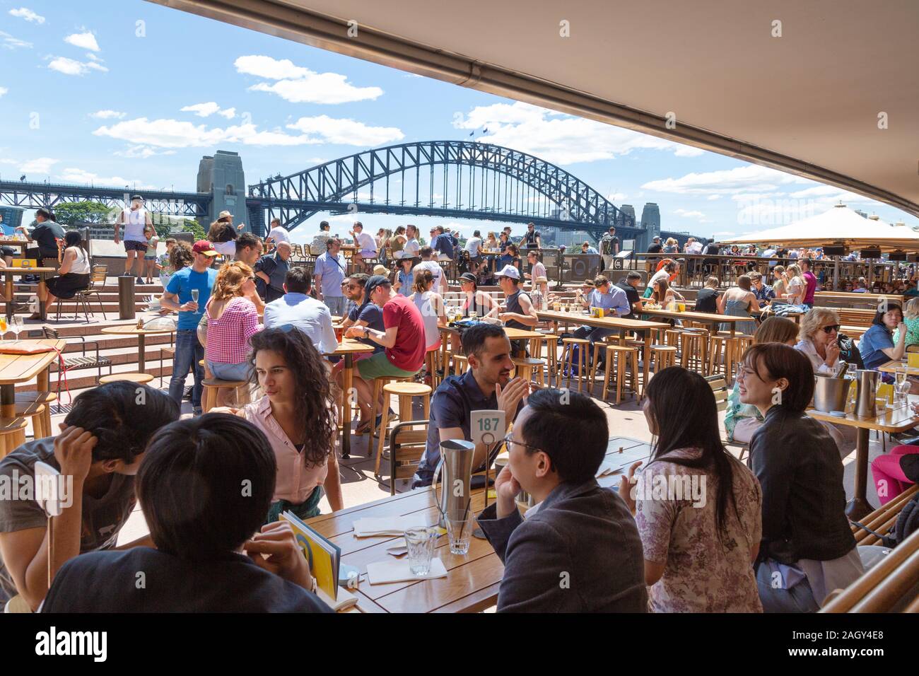 Stile di vita di Sydney; bar e caffetteria di Sydney; persone che mangiano e bevono, l'Opera Bar sotto l'Opera House, con il Sydney Harbour Bridge, Sydney Australia Foto Stock