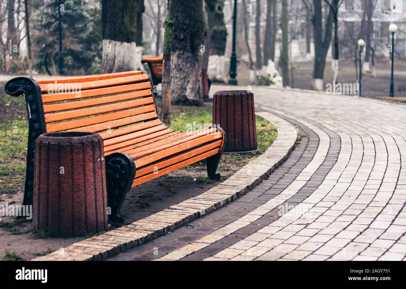 Orange panca in legno, granito spazzatura e passeggiata nel parco di autunno in un giorno di pioggia Foto Stock