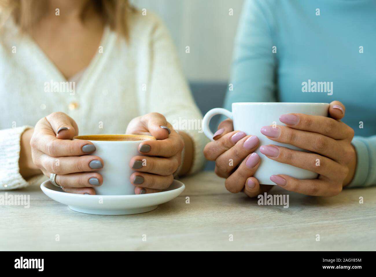 Le mani di due giovani femmine amichevole in informale azienda tazze di caffè Foto Stock