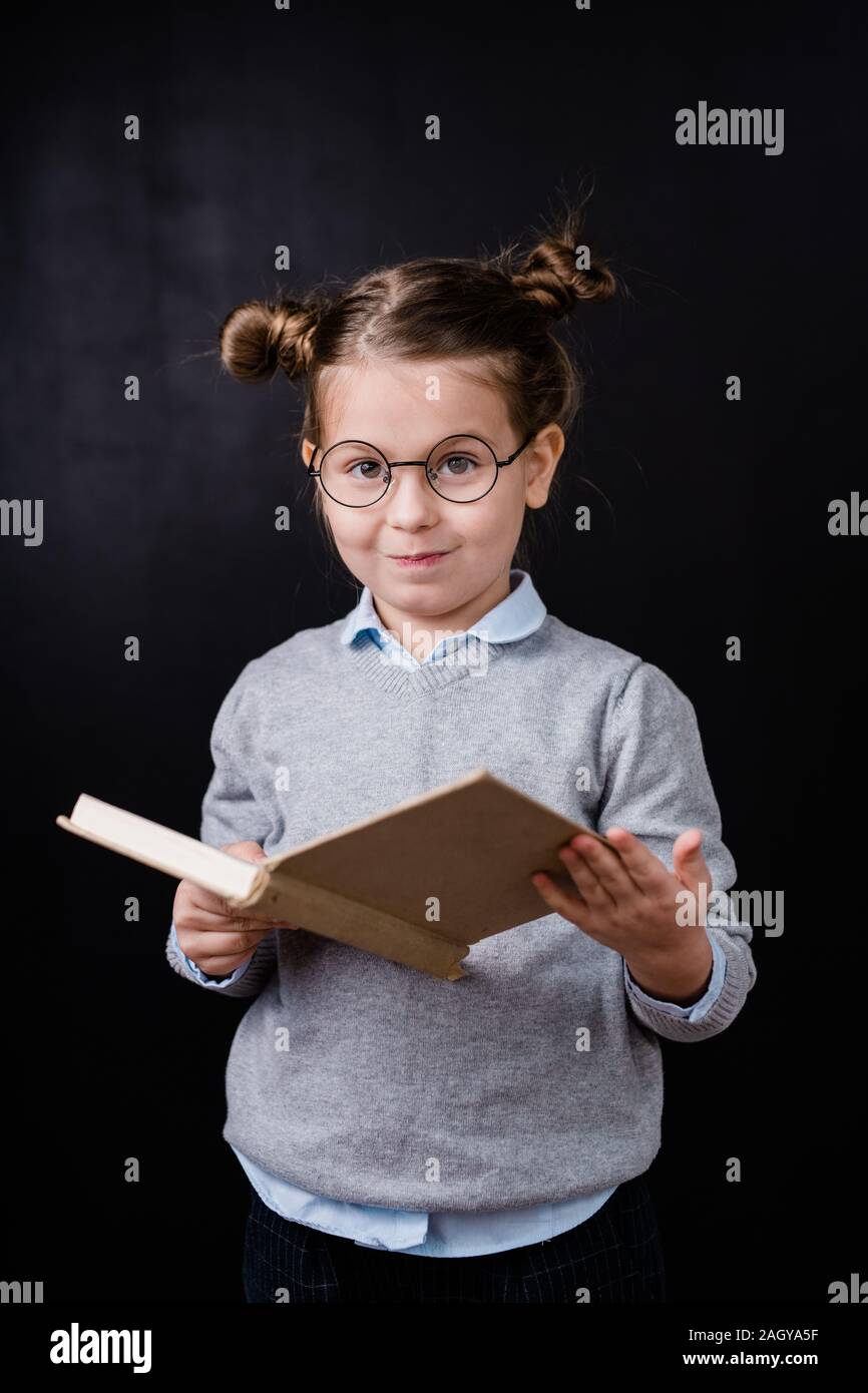 Adorabili schoolgirl elementari in occhiali lettura libro nella parte anteriore della fotocamera Foto Stock