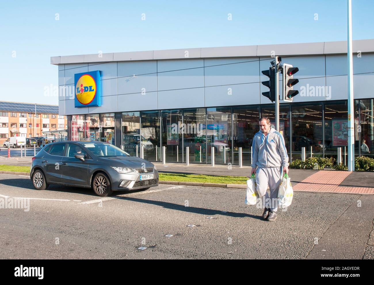 Di recente costruzione negozio Lidl in Blackpool i costi di vendita cuttring elementi quali bevande, alimentare ecc. Uomo con lo shopping bnags strada di attraversamento.su un attraversamento dei Puffini. Foto Stock