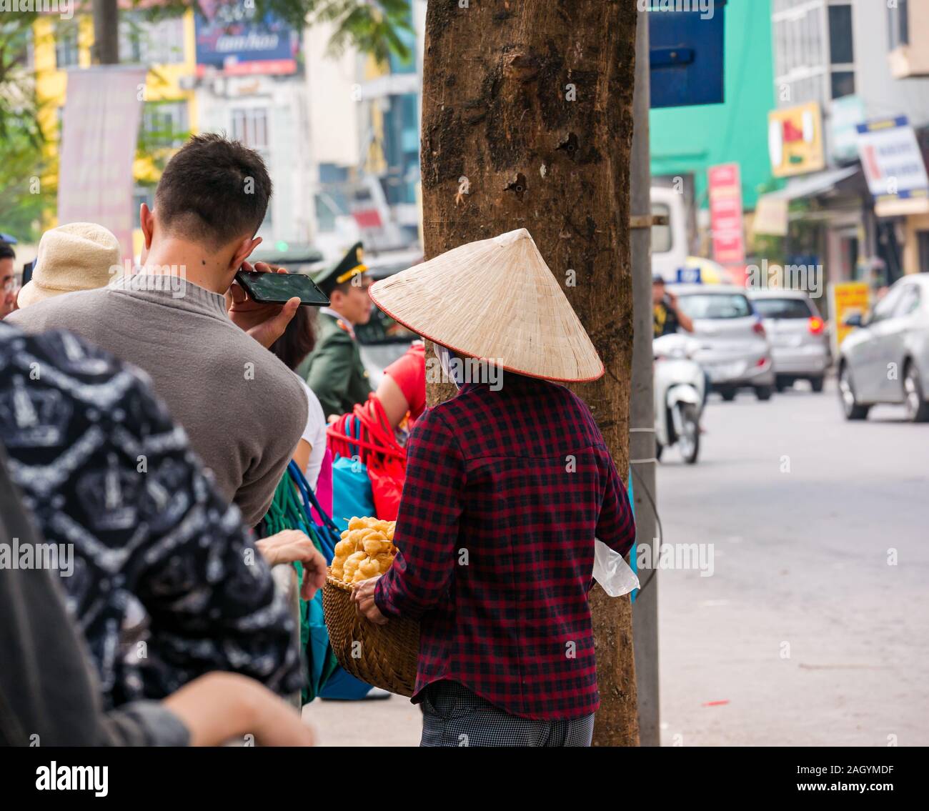 Il vietnamita donna che indossa cappello conico di vendita di alimenti su strada di persone in piedi in coda, Hanoi, Vietnam Asia Foto Stock