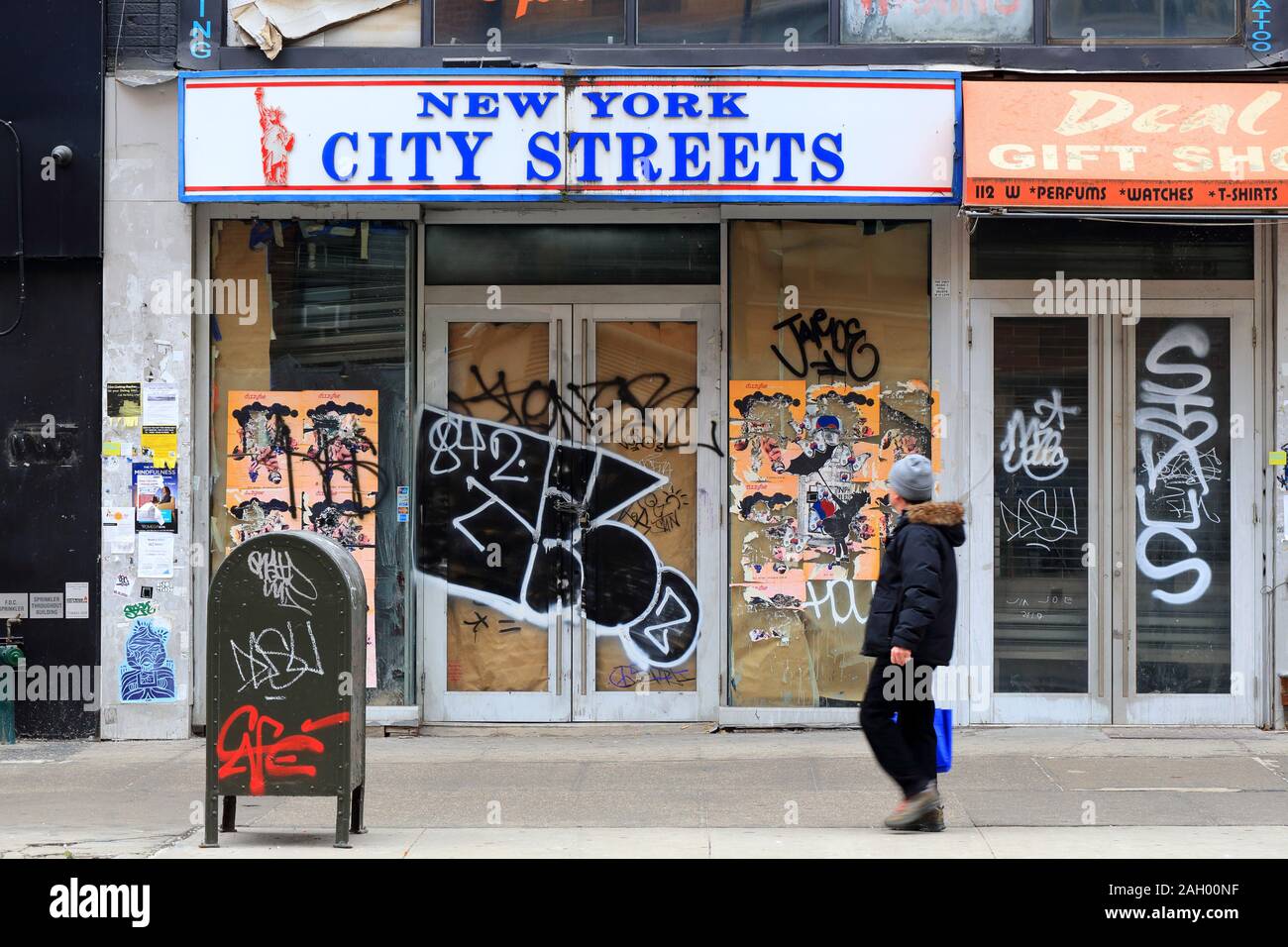 Una persona che cammina davanti a un vacante, imbarcato fino alla vetrina coperta di graffiti nella città di New York Foto Stock