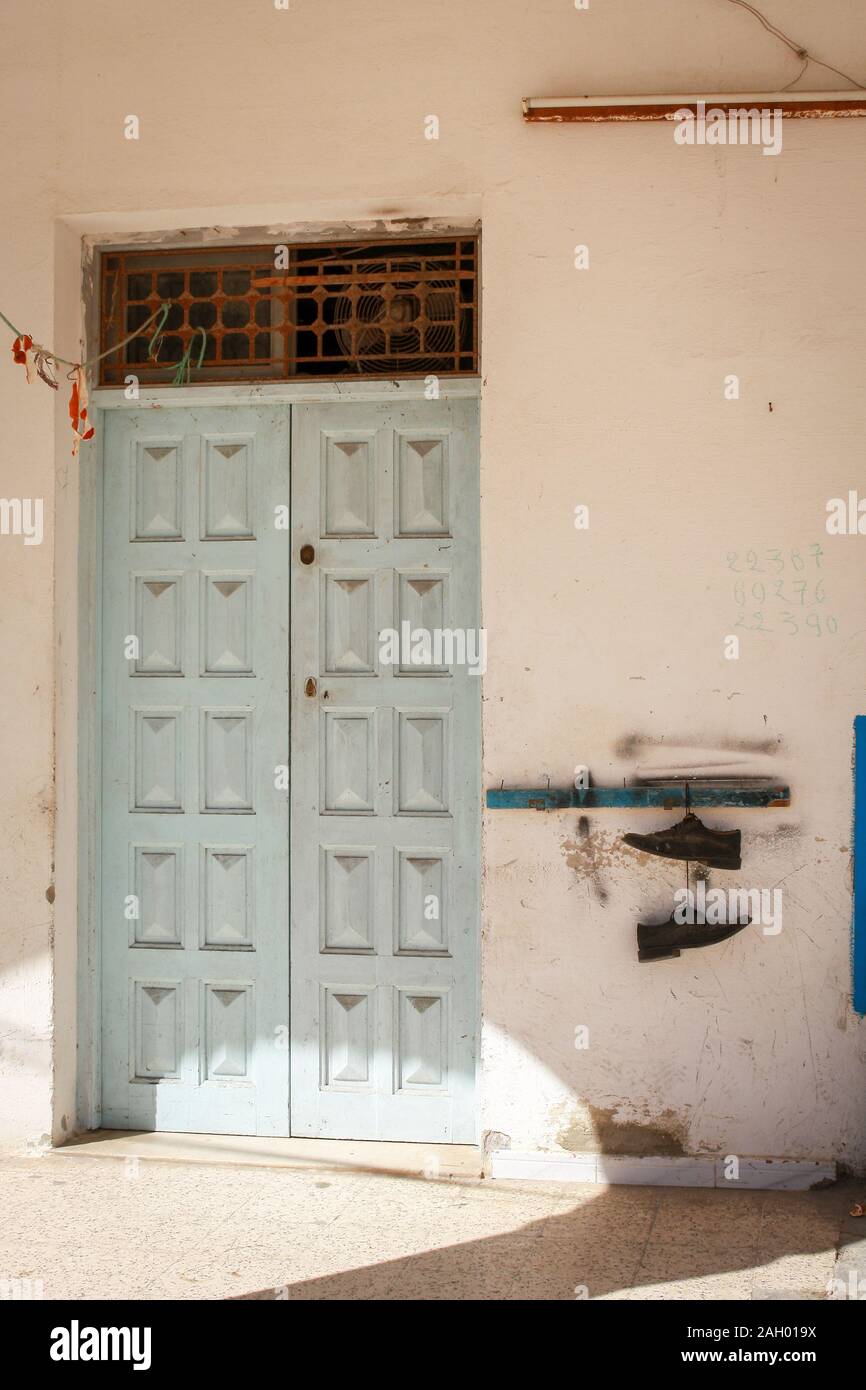 Porta blu chiaro all'edificio dipinto di bianco a Monastir, Tunisia. Un paio di scarpe vecchie è appeso appena fuori dalla porta. Foto Stock