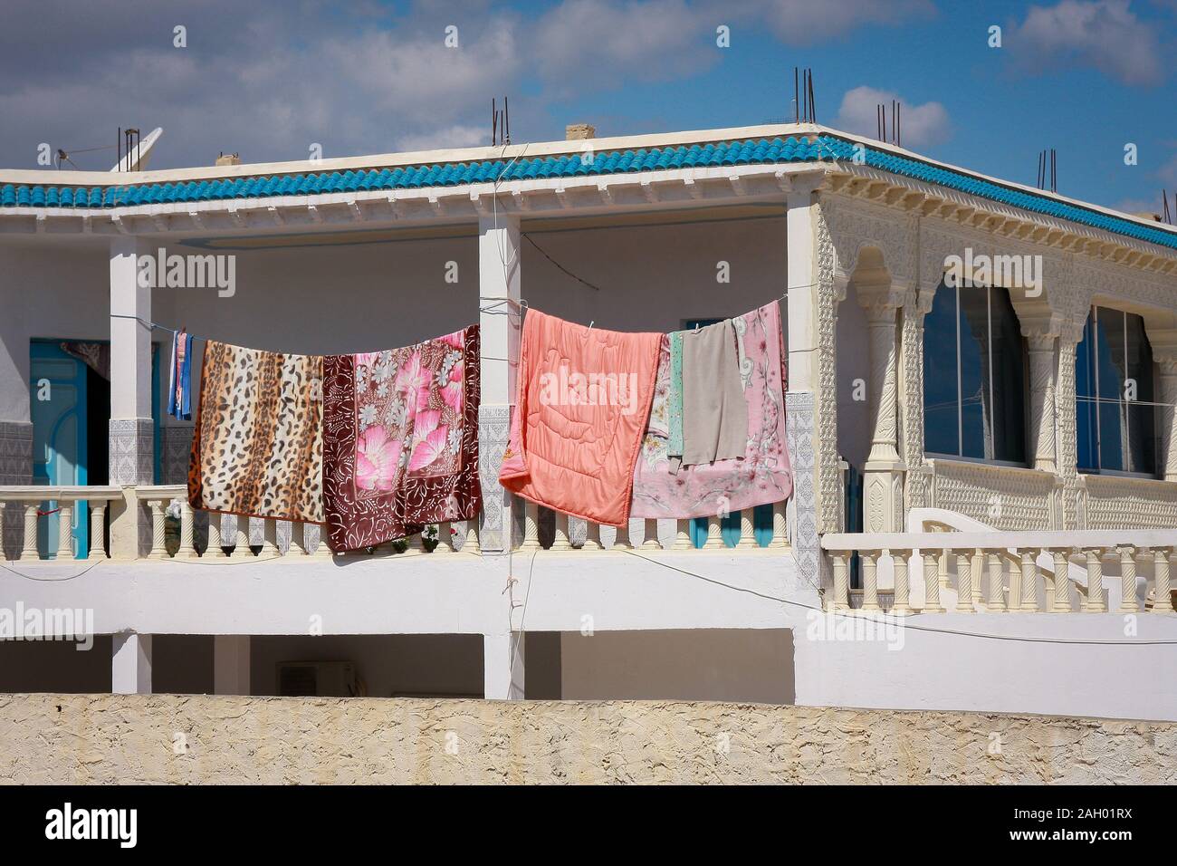 Lenzuola colorate e un piumone si asciugano sul balcone della casa nel sole forte del sole del mattino a Hergla, Tunisia Foto Stock