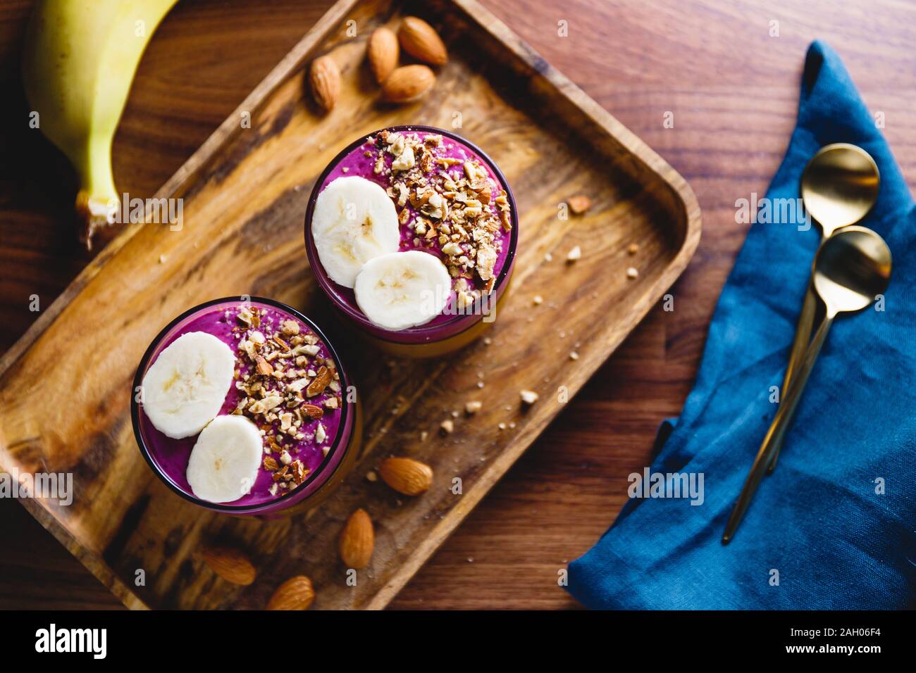 Vista dall'alto di due bicchieri con violet berry e frullato di banane sono serviti di mandorle schiacciate su un vassoio in legno Foto Stock