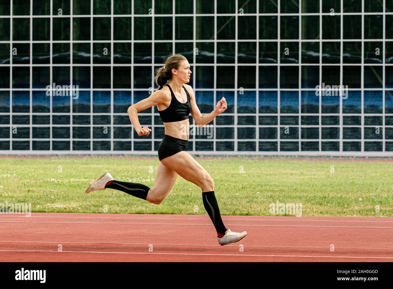 Atleta femminile in scarpe di picchi di via di corsa stadium di sfondo di edificio con facciata in vetro Foto Stock