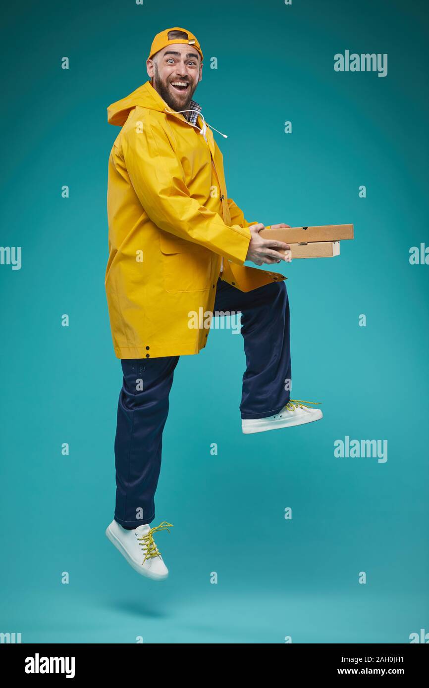 Studio pieno colpo di allegro Consegna del cibo uomo indossa uniformi giallo jumping con pizzaa scatole in mani Foto Stock