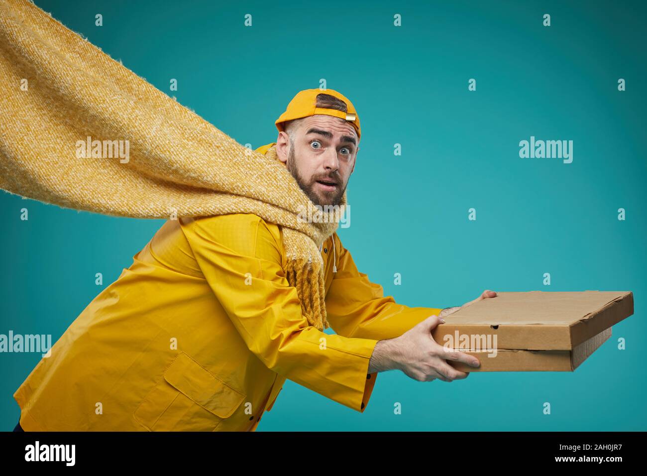 Di medie studio shot di pizza consegna uomo lo scivolamento e la caduta verso il basso, sullo sfondo turchese Foto Stock