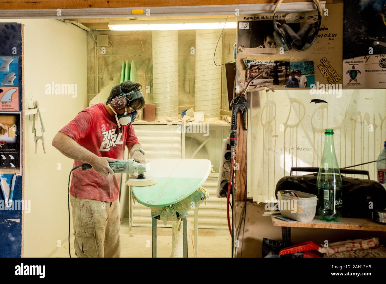 Uomo con maschera la levigatura di una tavola da surf in un polveroso shop Foto Stock