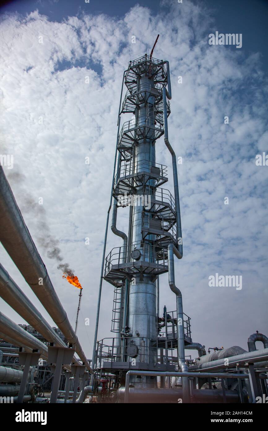 Grigio a colonne di distillazione e strutture metalliche di una raffineria di petrolio pianta nel deserto. Fiamma di fuoco torcia a gas. Cielo blu con nuvole di luce. Foto Stock