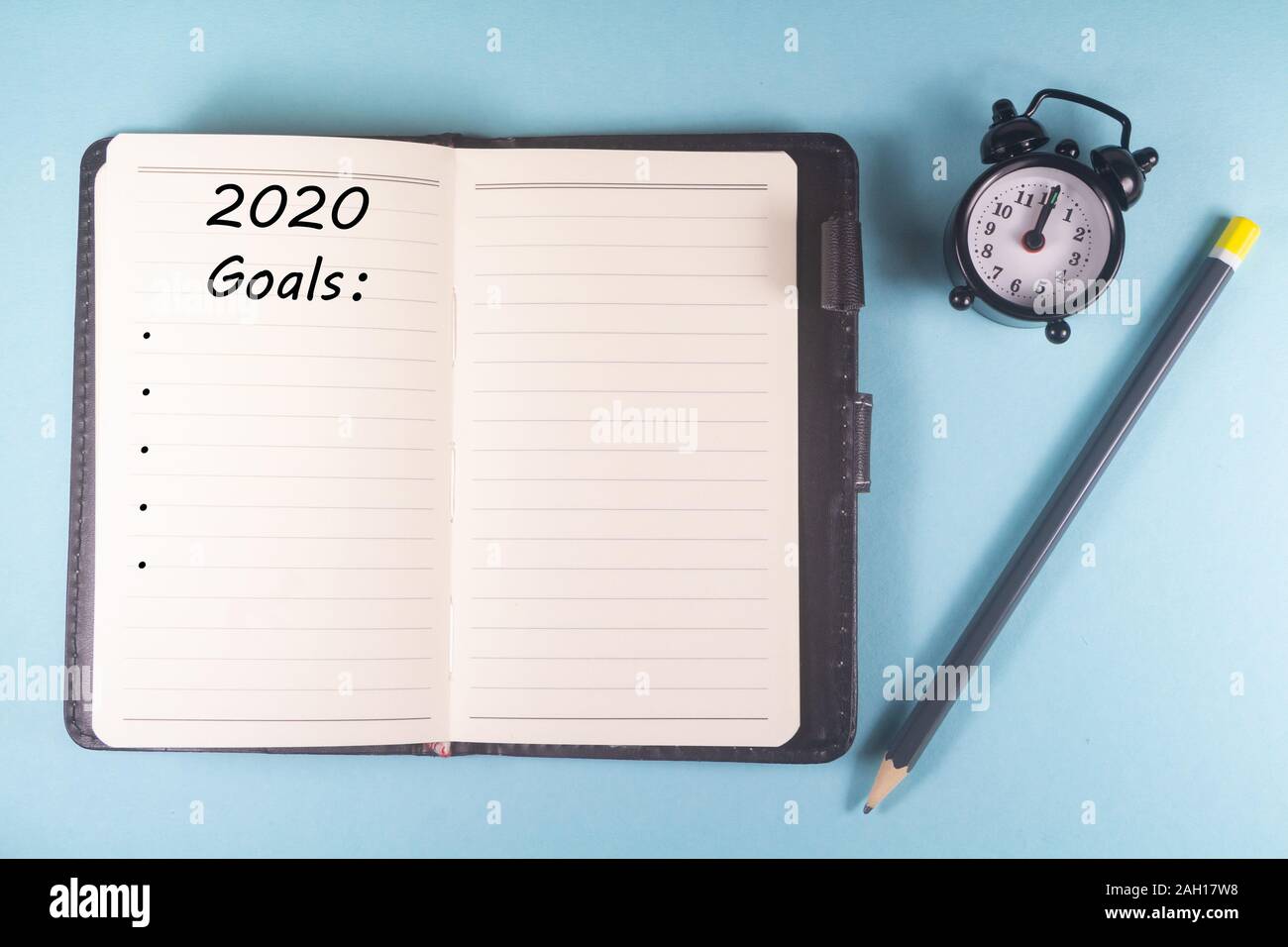 Matita, notebook con 2020 obiettivi e sveglia su sfondo blu Foto Stock