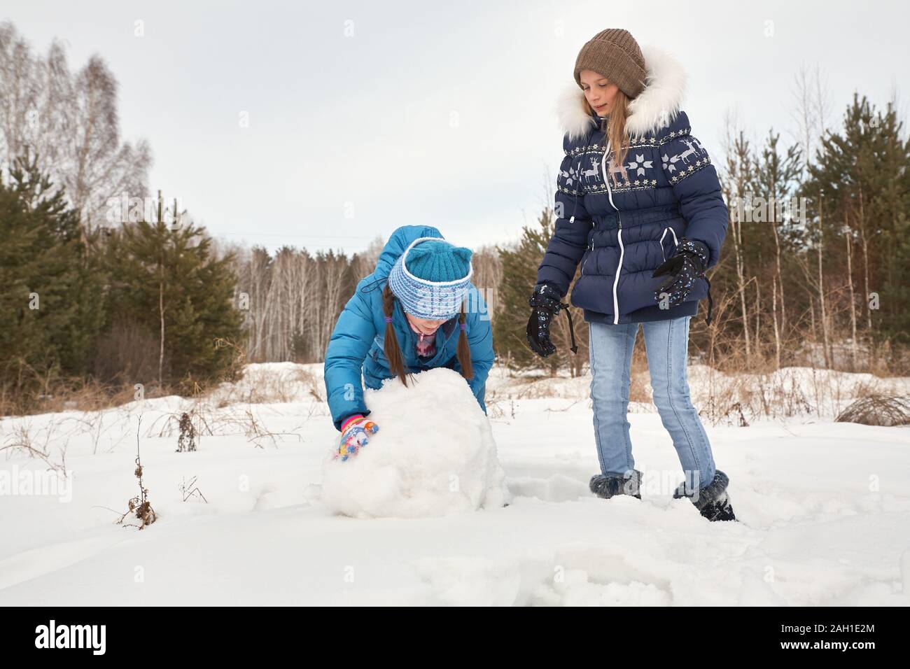 due amici femminili che costruiscono un pupazzo di neve. ragazze divertenti su una passeggiata in inverno all'aperto. Foto Stock