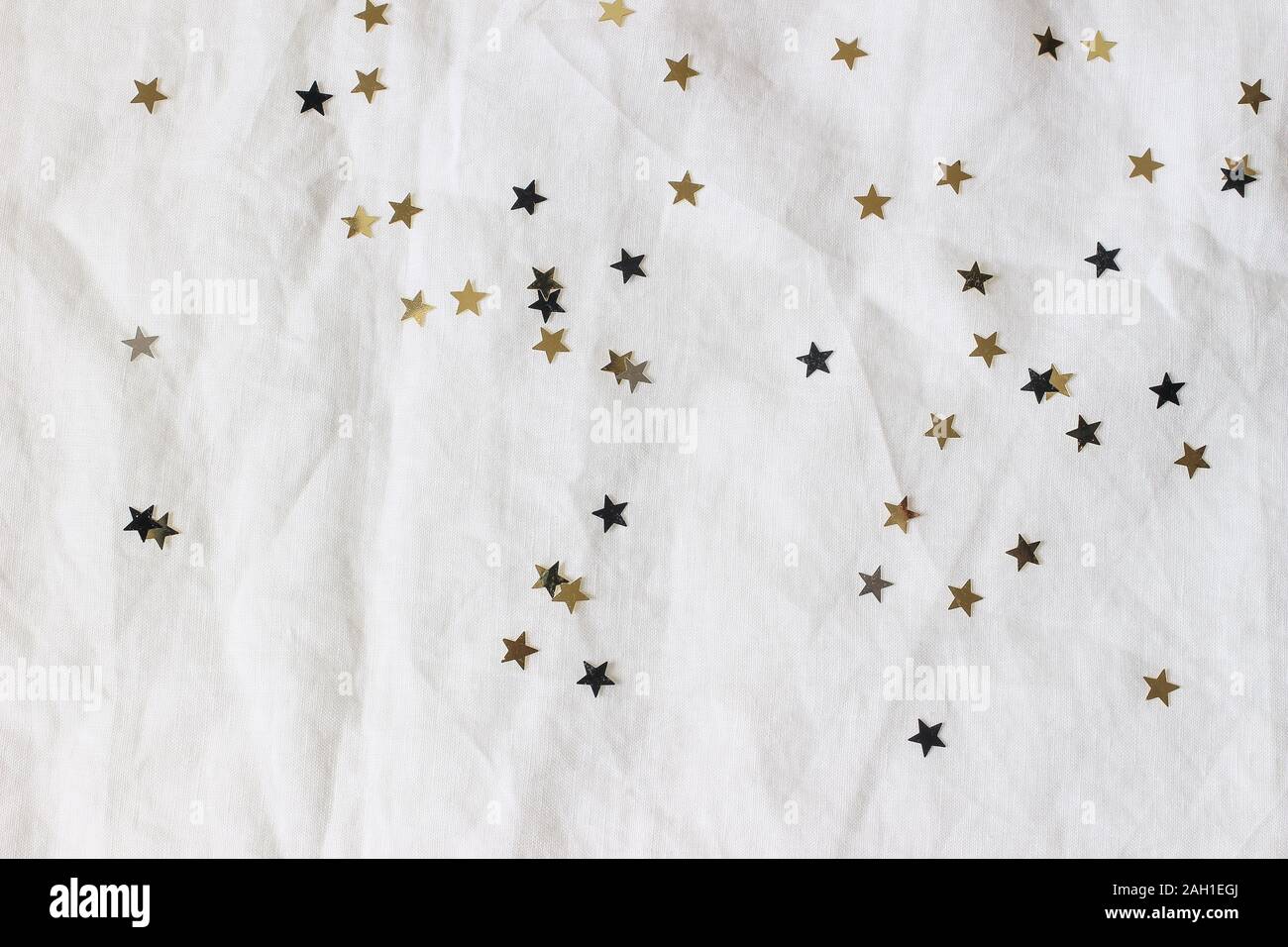 Natale e Anno Nuovo composizione. Golden decorativo e nero coriandoli stelle su tovaglie bianche tovaglie sfondo. Festa di compleanno il concetto di partito. Foto Stock