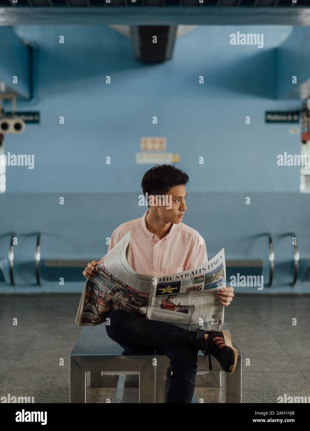 Singaporean male in Pink Shirt, The Straits Times Newspaper at Queenstown MRT, Rightward Glance, Commuter Lifestyle, Daily Reading, trasporti pubblici Foto Stock