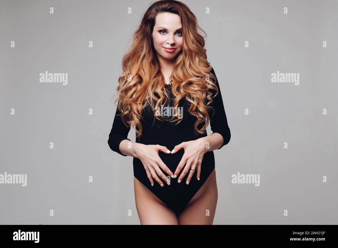 Sorridente piuttosto madre in attesa che pongono in black body in studio Foto Stock