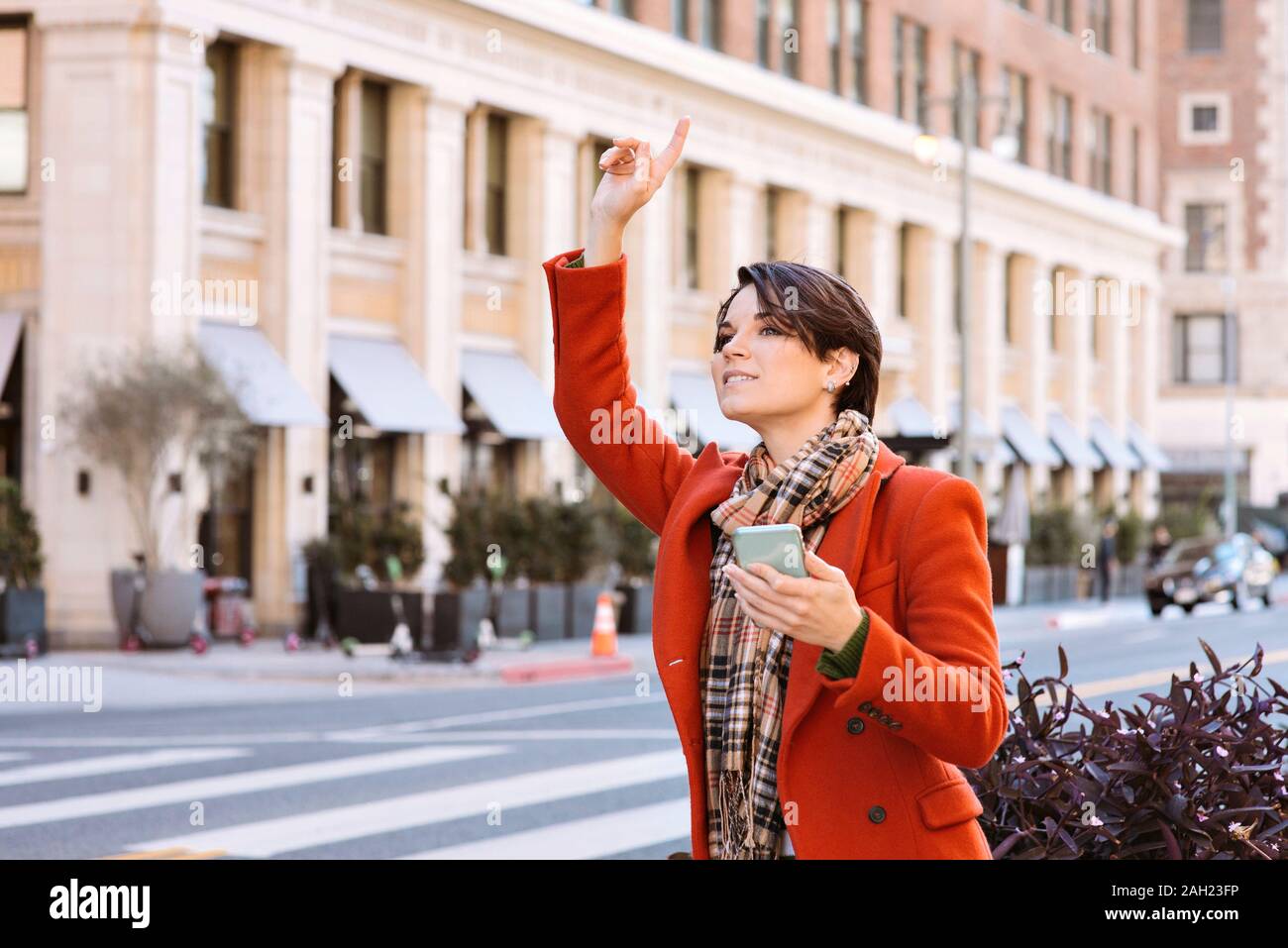 Giovane bella femmina richiede una corsa da un uber driver su una strada di città mentre si tiene un telefono cellulare Foto Stock