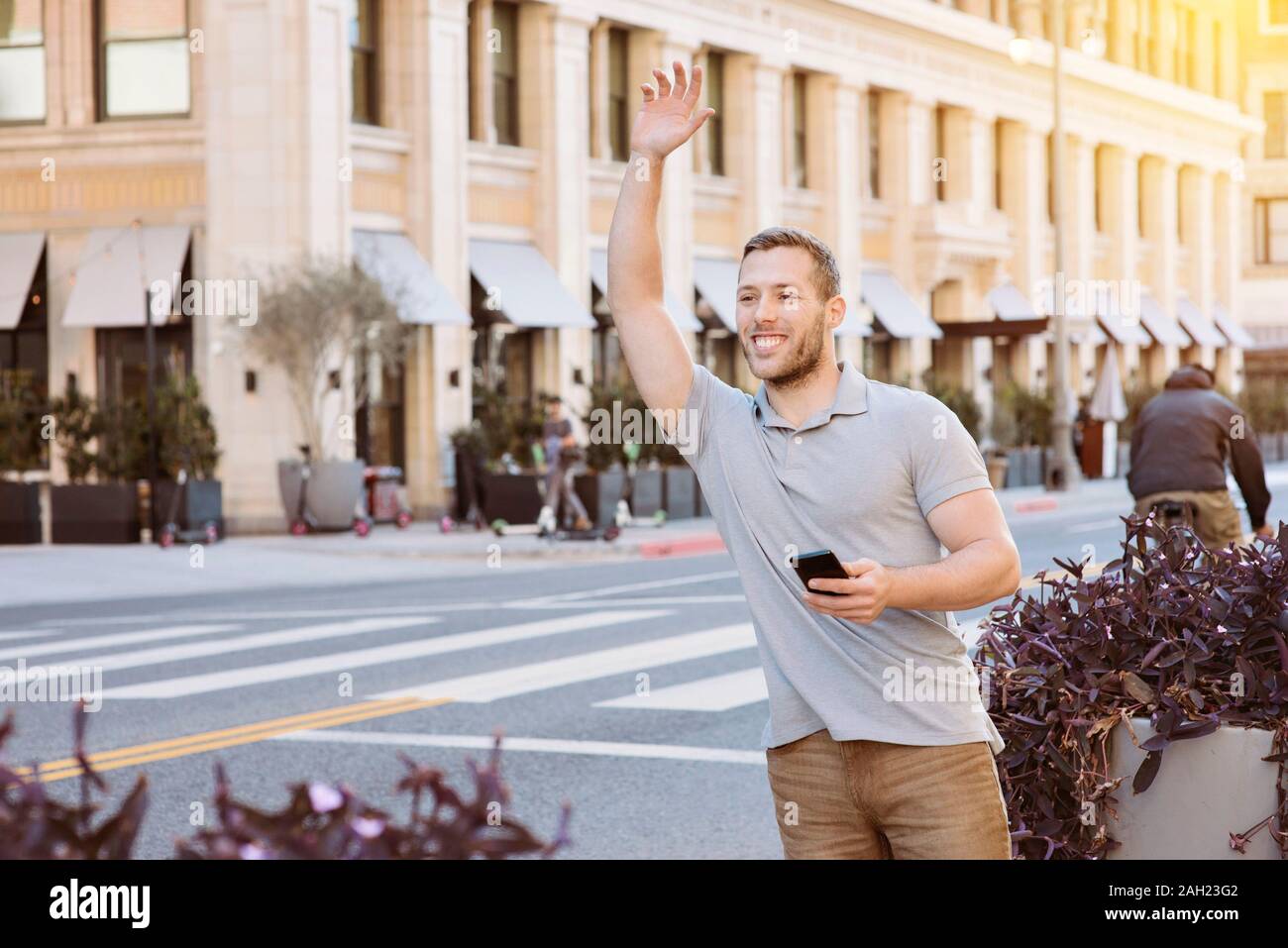 Maschio bianco con un sorriso chiede un driver uber mentre si tiene il suo telefono cellulare in città su un luminoso giorno Foto Stock
