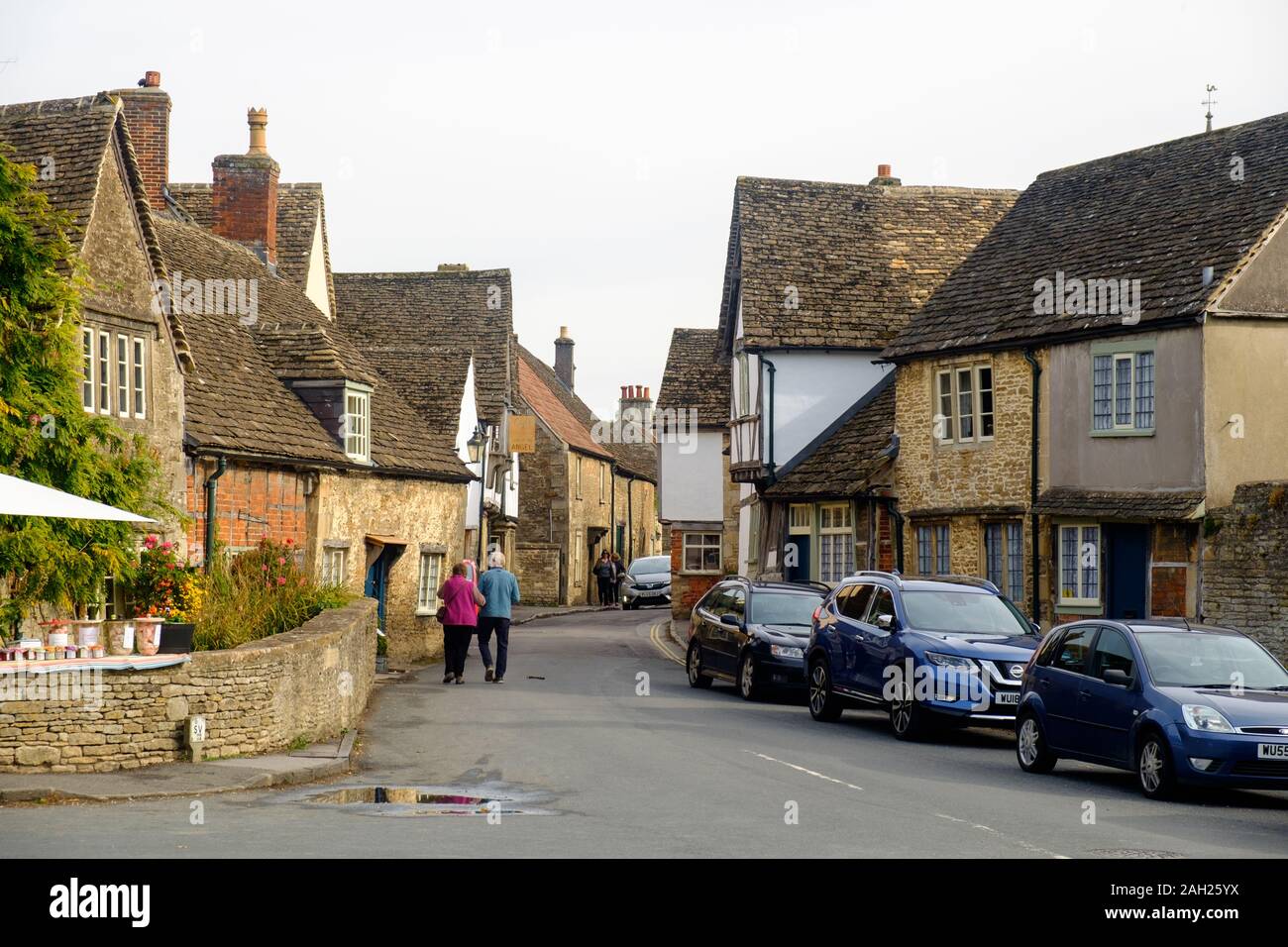 Una coppia senior va a braccetto attraverso le strade di Lacock, un piccolo villaggio con case tradizionali. Questa posizione serve spesso come set di un film. Foto Stock