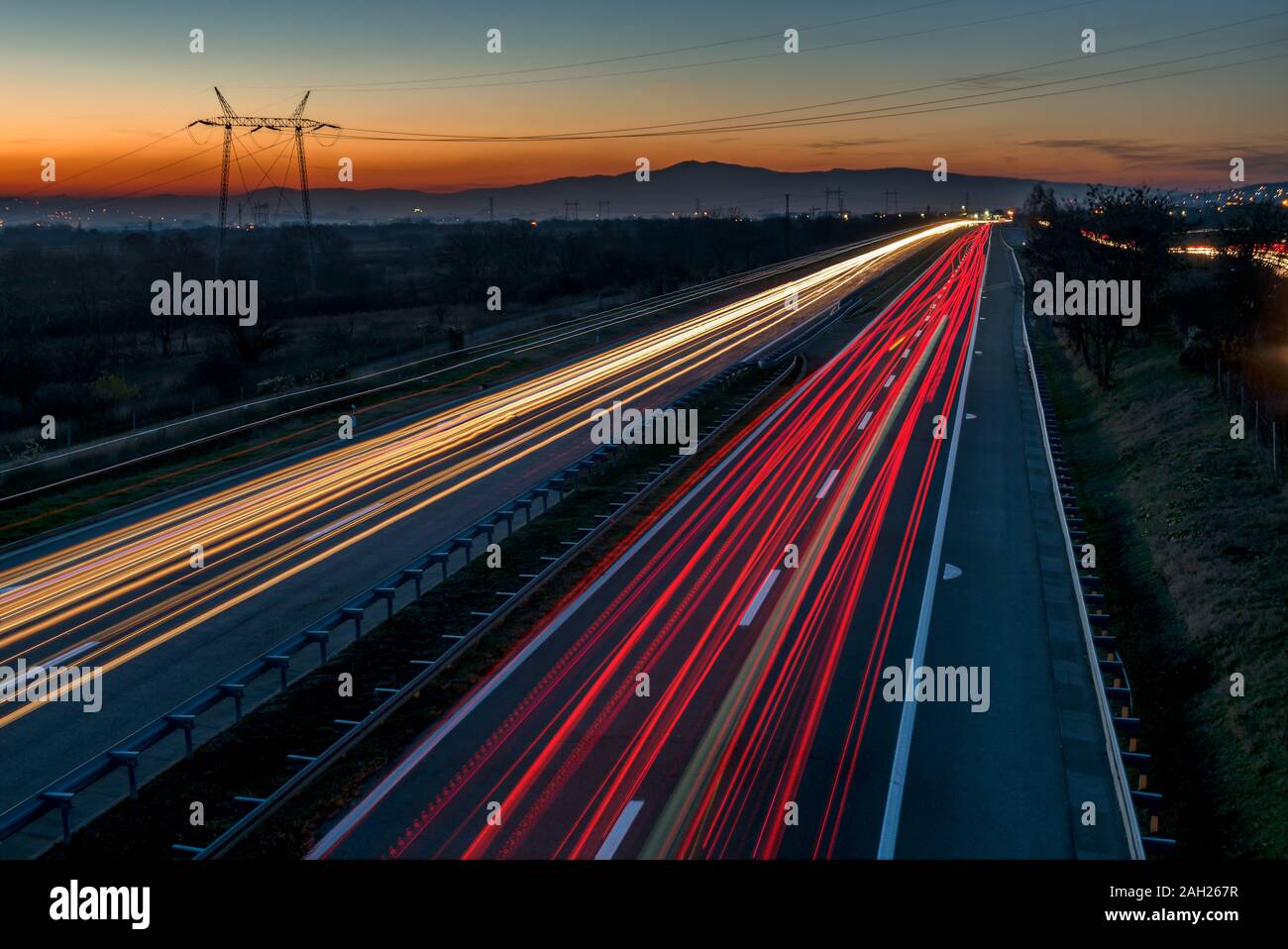 Auto sentieri di luce su una autostrada dritto al tramonto. Di notte i percorsi di traffico, motion blur, Night city road con traffico moto faro. Foto Stock