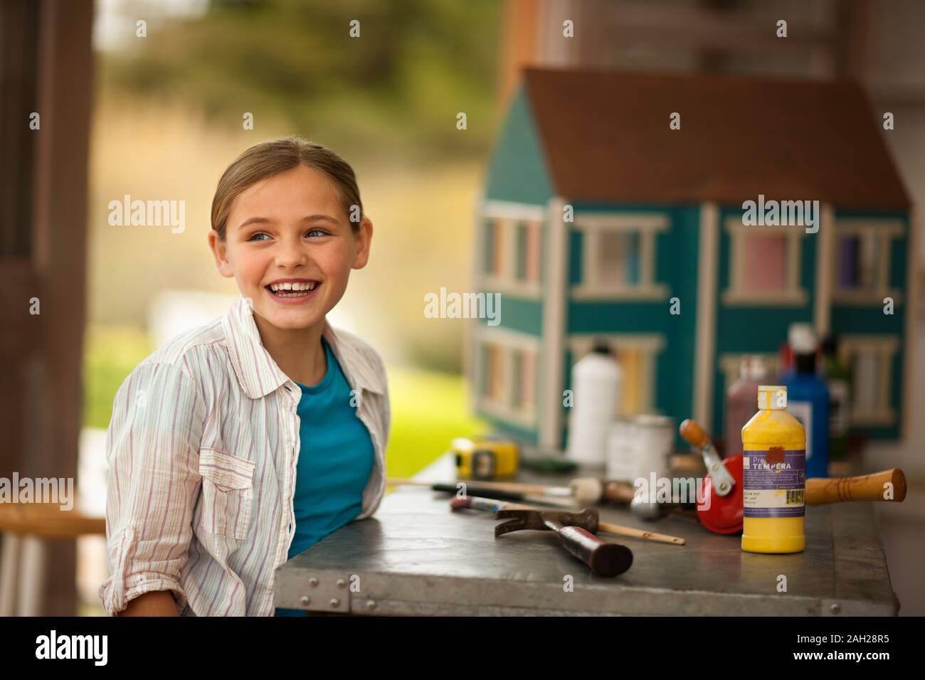 Ridere ragazza seduta accanto a un banco di lavoro pieno di strumenti artigianali all'interno di un garage. Foto Stock