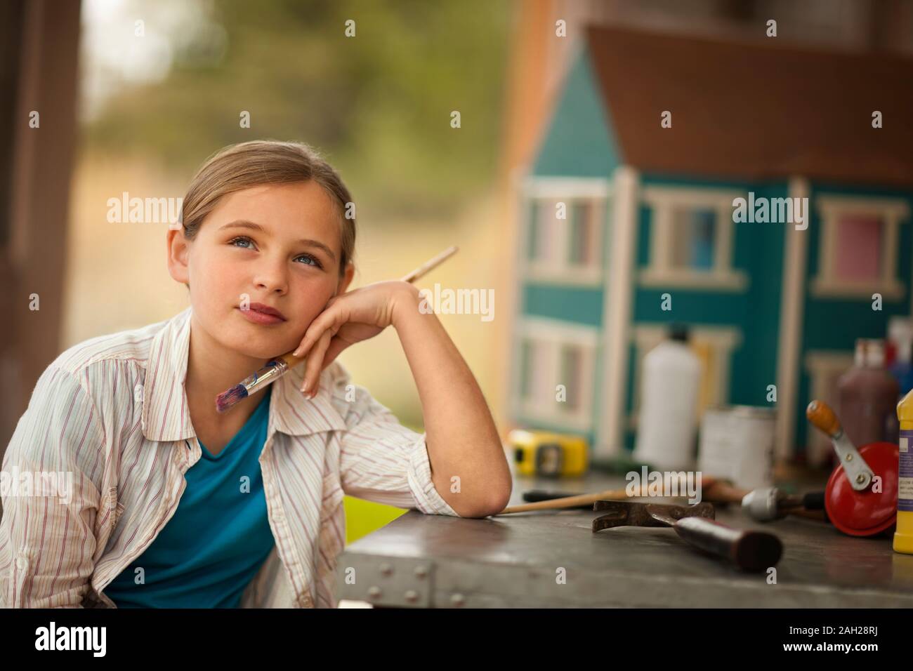 Ragazza fantasticando tenendo un pennello accanto a un banco di lavoro all'interno di un garage. Foto Stock