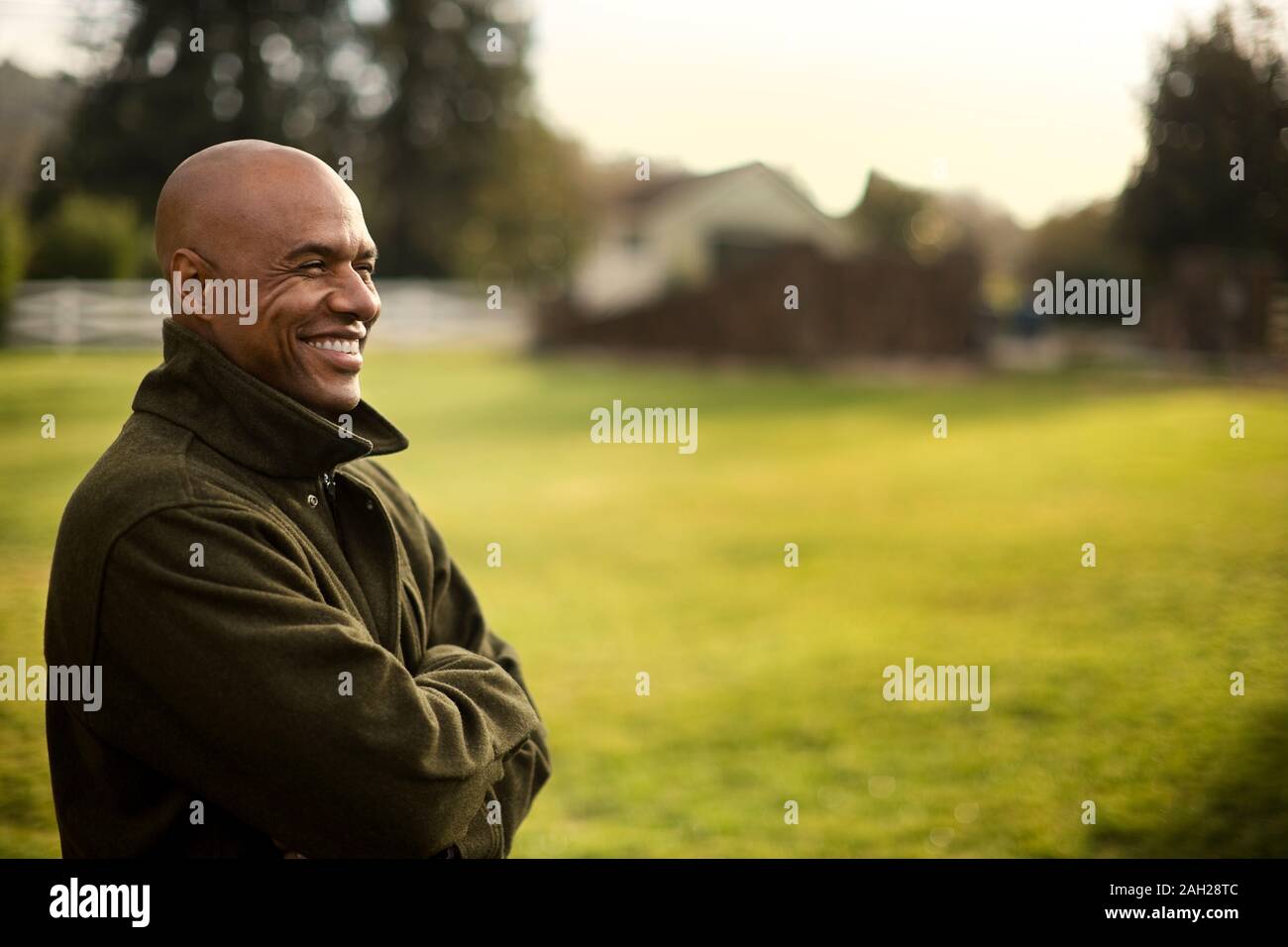 Sorridente metà uomo adulto in piedi in un parco con le braccia incrociate. Foto Stock