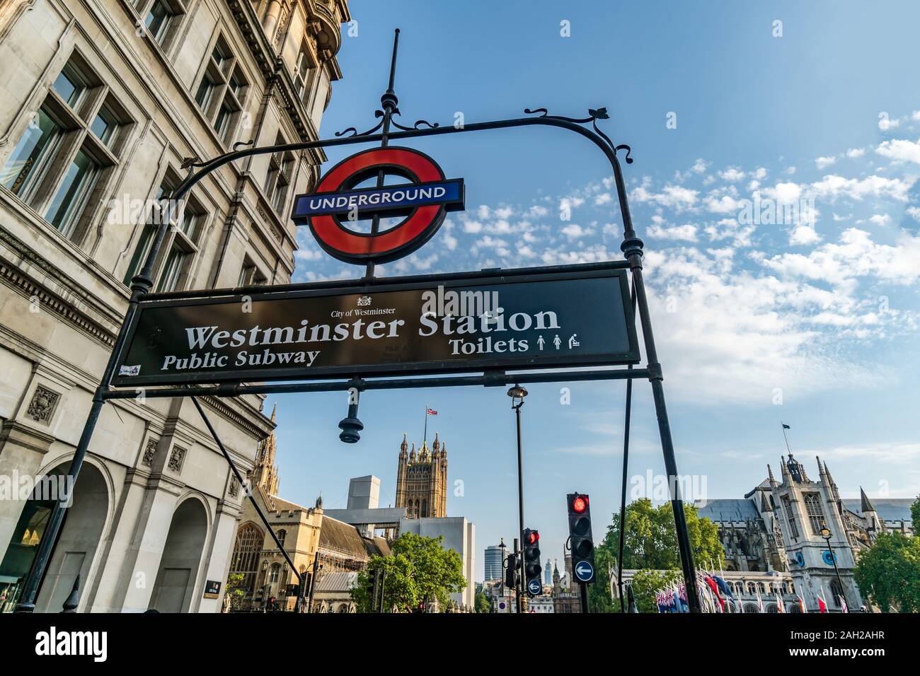 Il segno della stazione della metropolitana di Westminster con la Casa del Parlamento e la Westminster Abbey in background, Londra, Inghilterra, GB Foto Stock