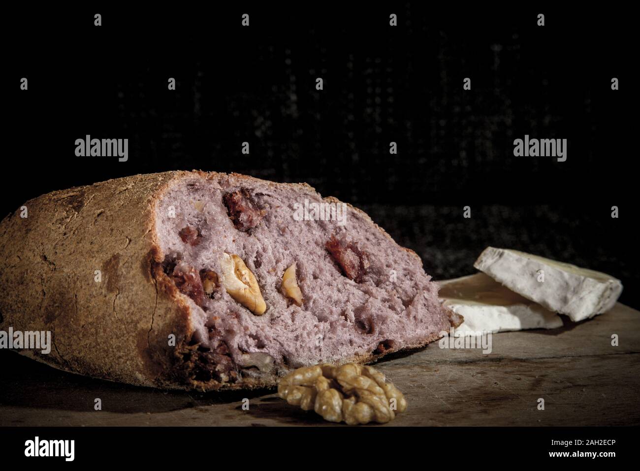 Il vino aromatizzato (pane pain au vin) con il suo tipico colore rosso all'interno, farcito con noci, sul display su un ceppo di legno, accanto a fette di Brie fromage che Foto Stock